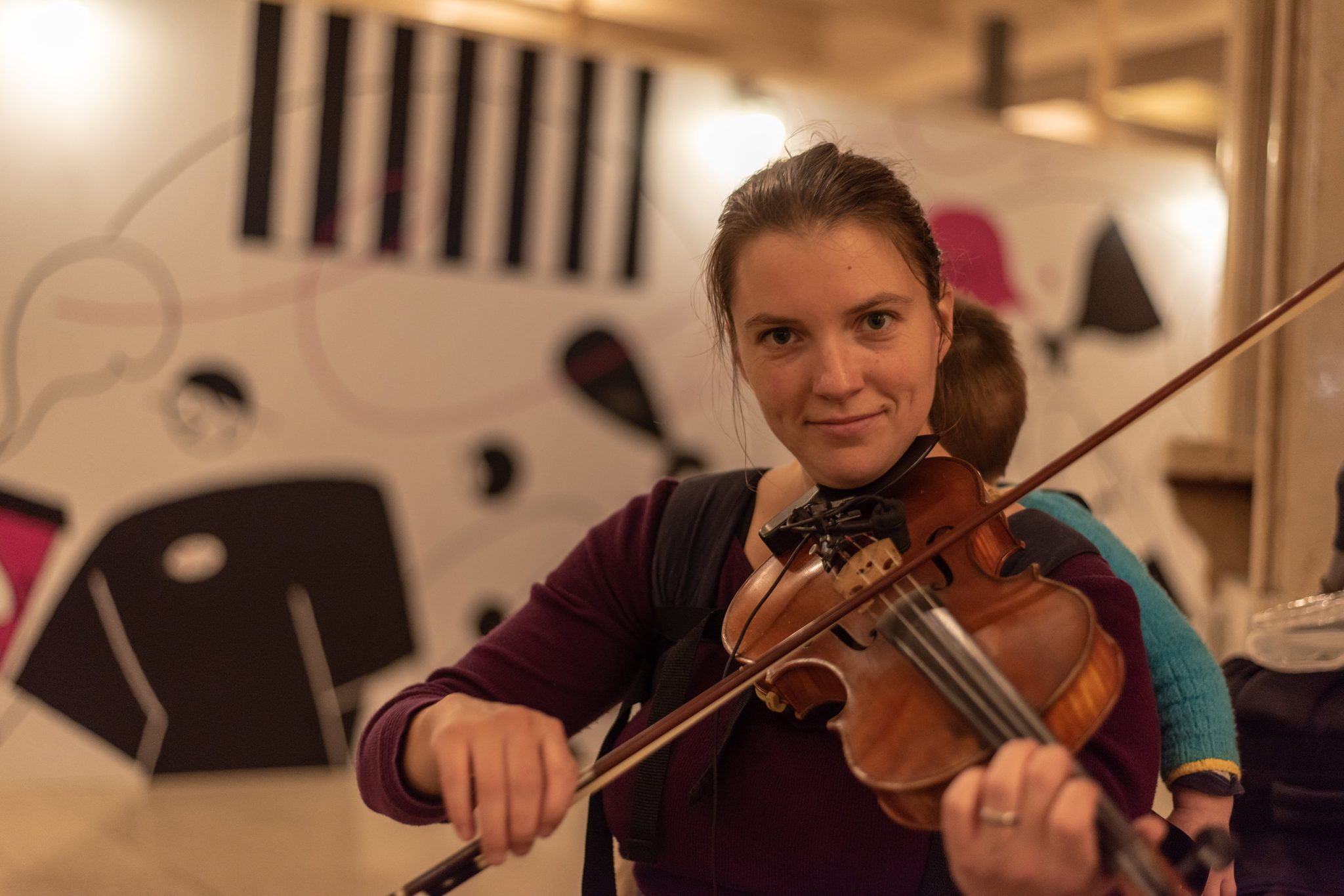 Naomi smiles over her fiddle while Ronin peeks out from over her shoulder.