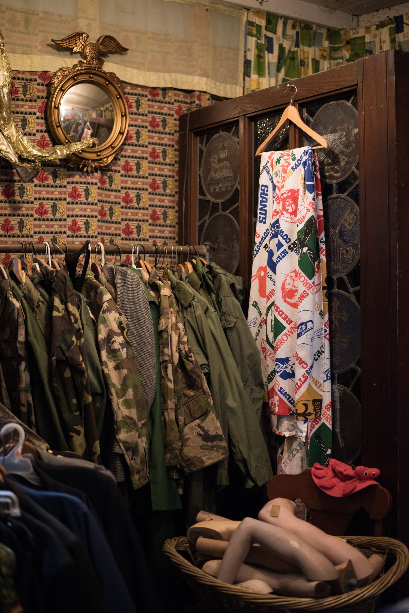 A thrift shop corner of army jackets, a gilt eagle mirror and a basket of mannequin legs.