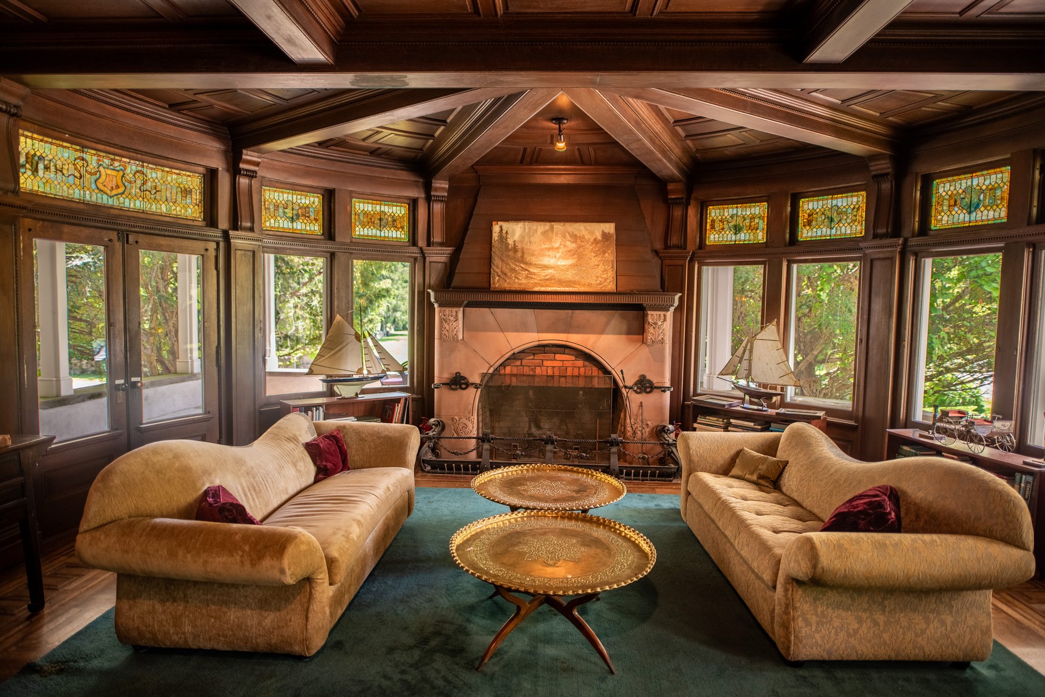 A beamed, paneled room with stained-glass transoms all the way around, two gold sofas facing a tiled fireplace.
