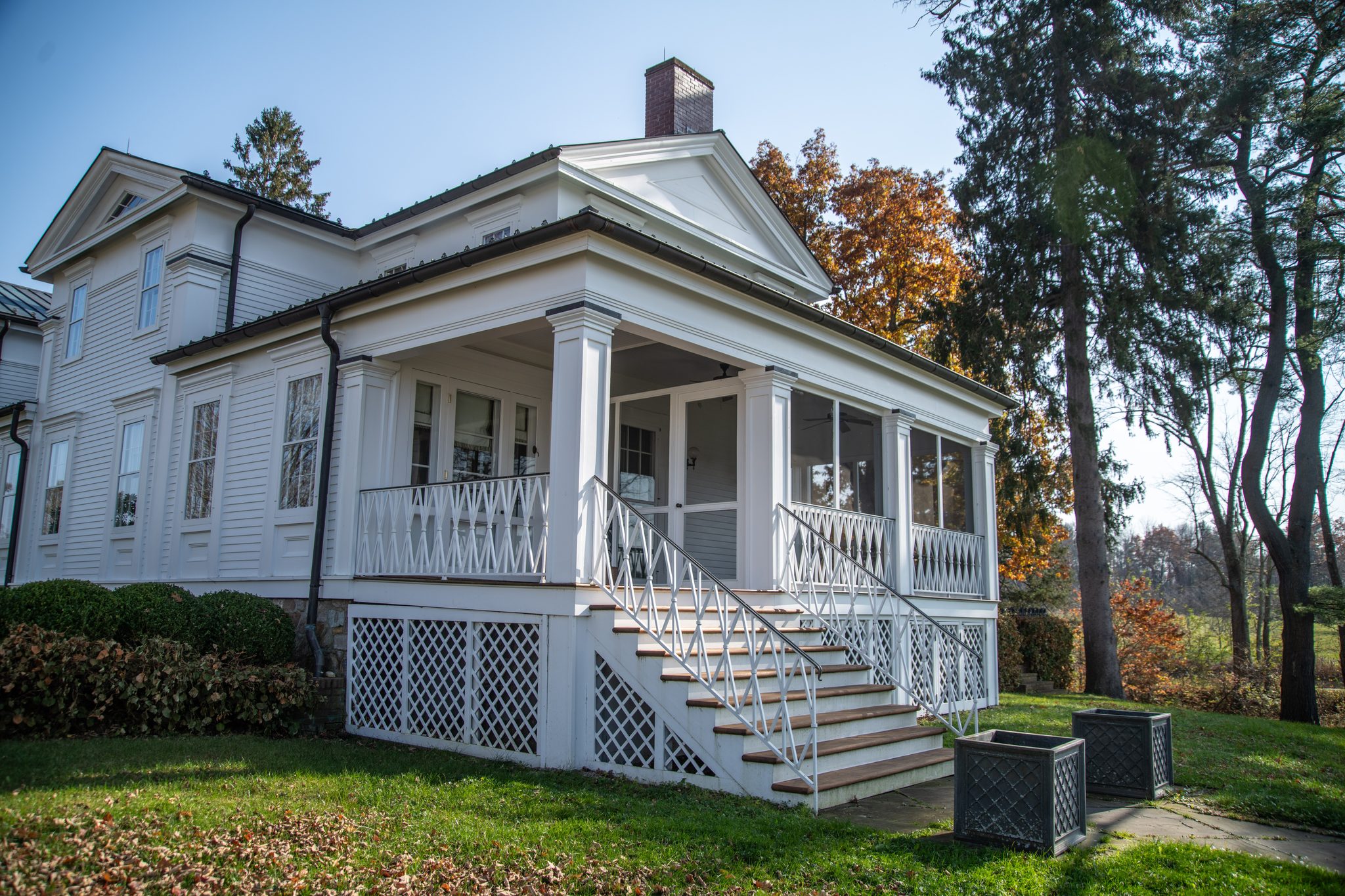 A lattice-skirted side porch with a chevron railing, lit by bright November sun and the last oak leaves.