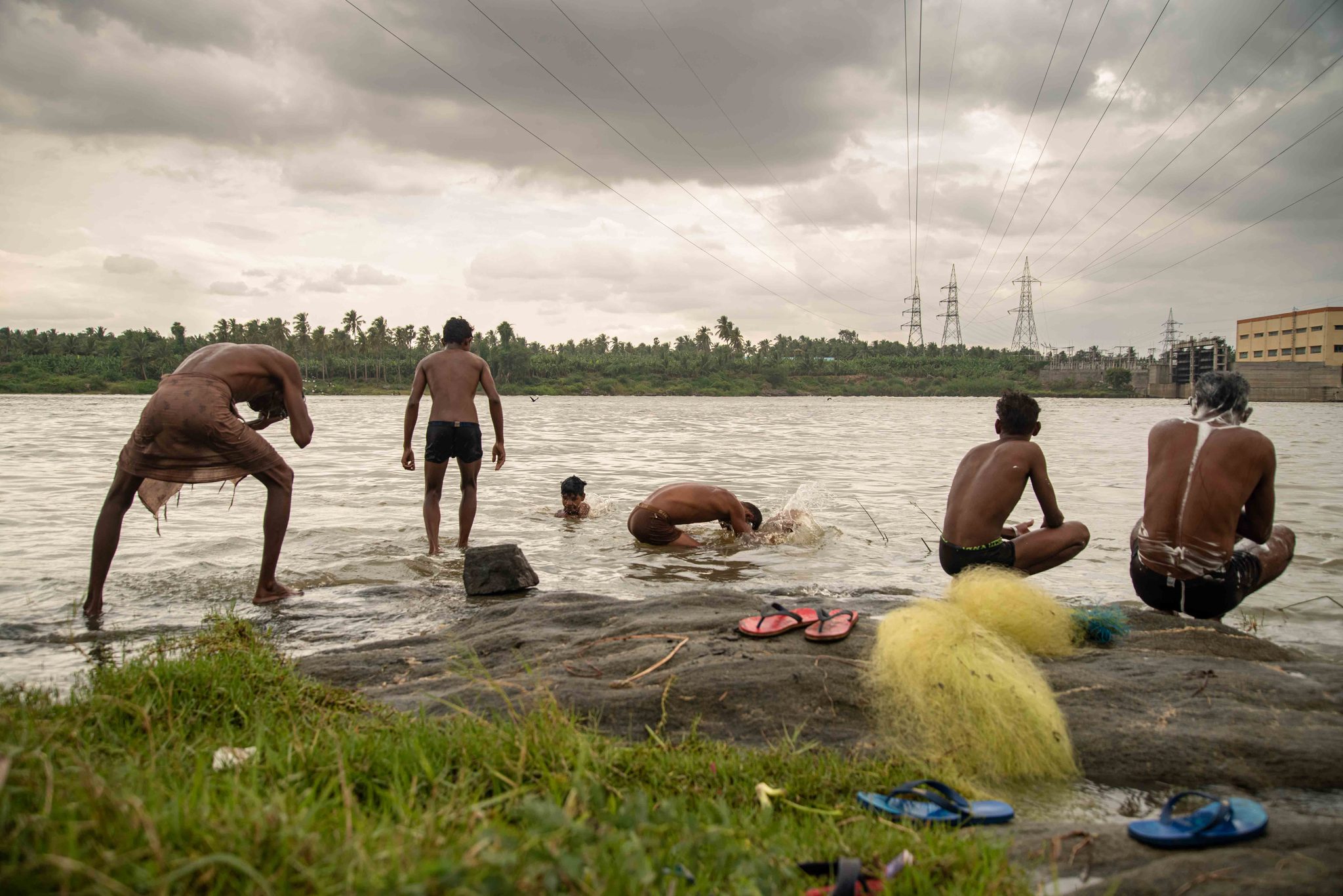 One man dips into the river while the others wash on the rocks.
