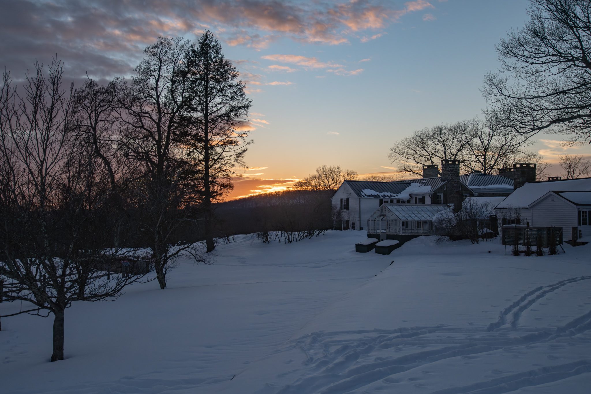 Sunset behind the farmhouse, bare trees in silhouette against the snow.