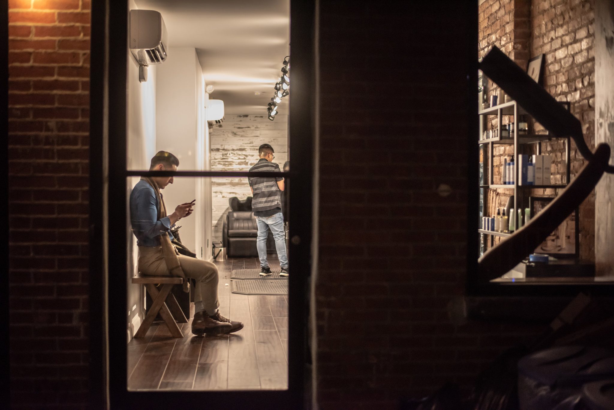Through the glass, a man waits his turn on the bench, phone in hand.