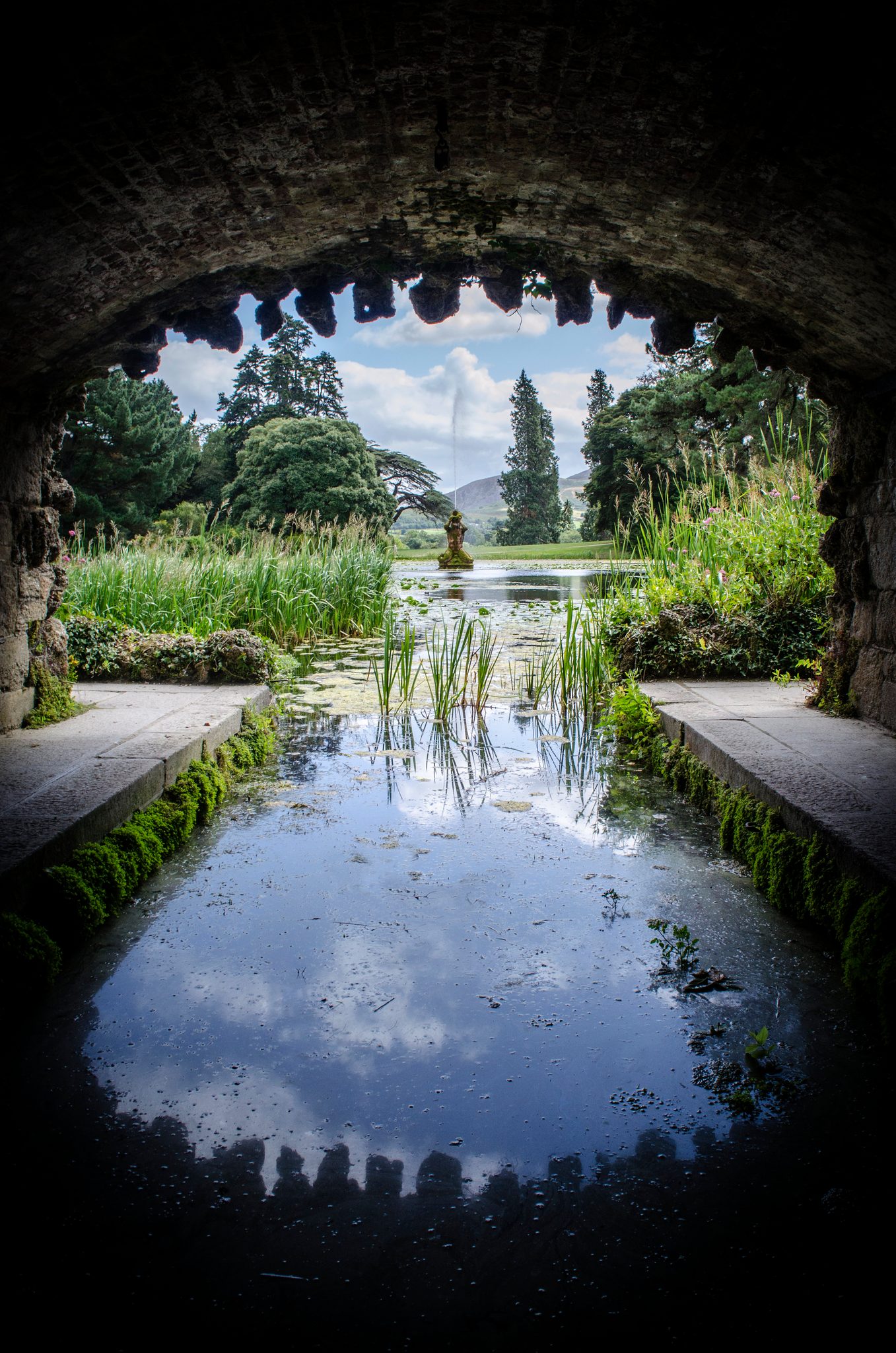 Through a stone arch, a garden pool mirrors the sky.