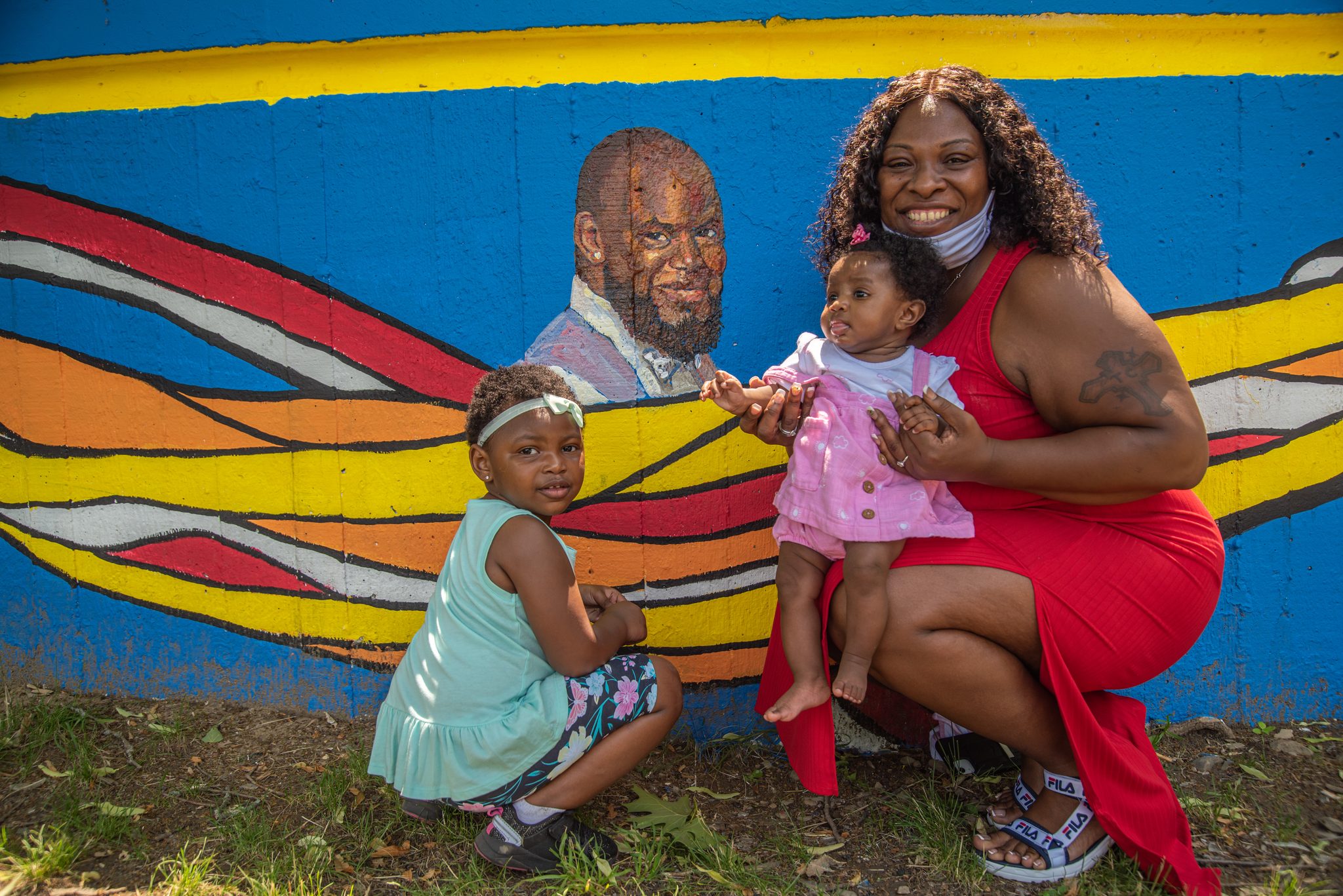 A family poses beside the mural's portrait, the baby in pink stealing the frame.