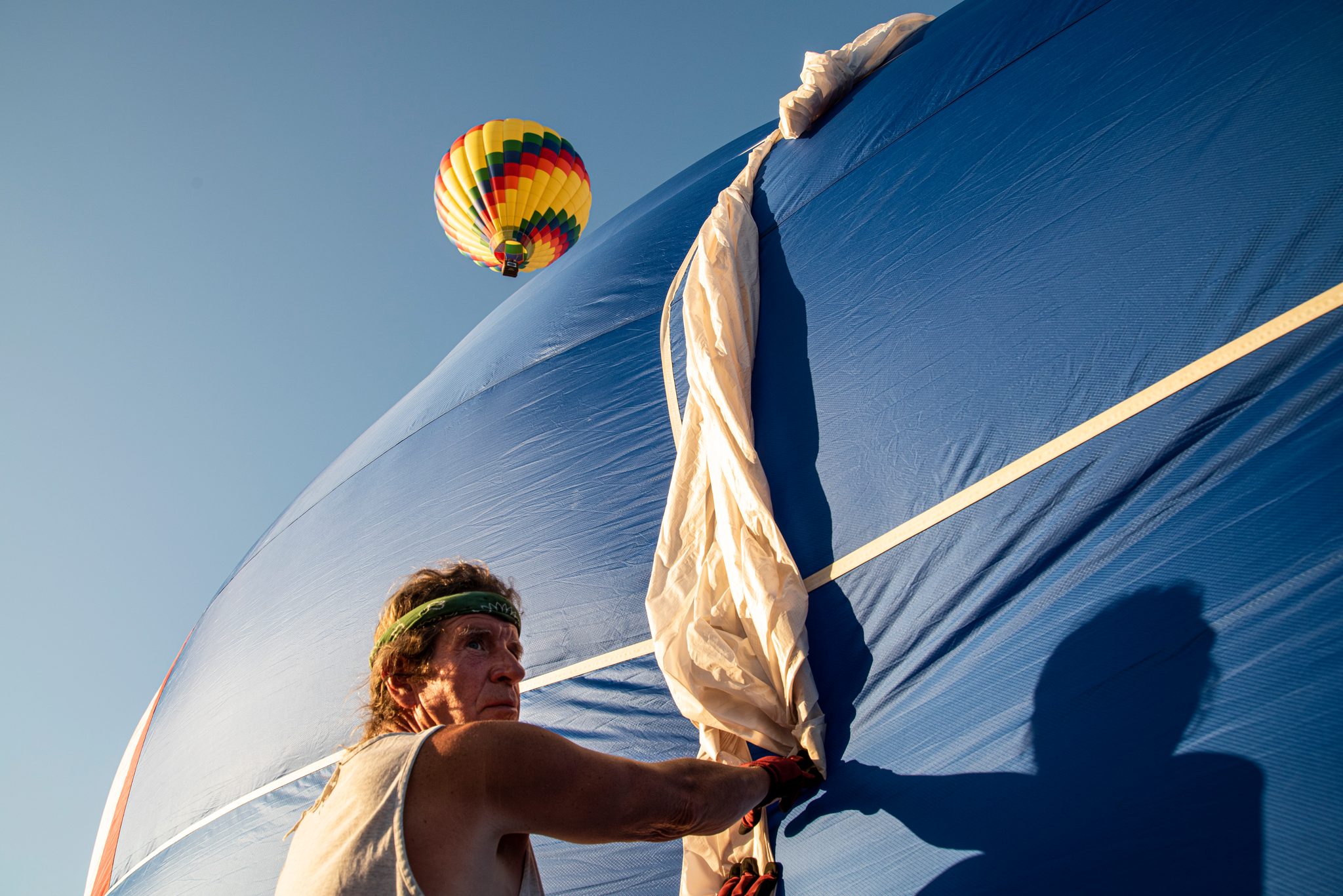 A crew member gathers the collapsing fabric, another balloon already rising in the sky.
