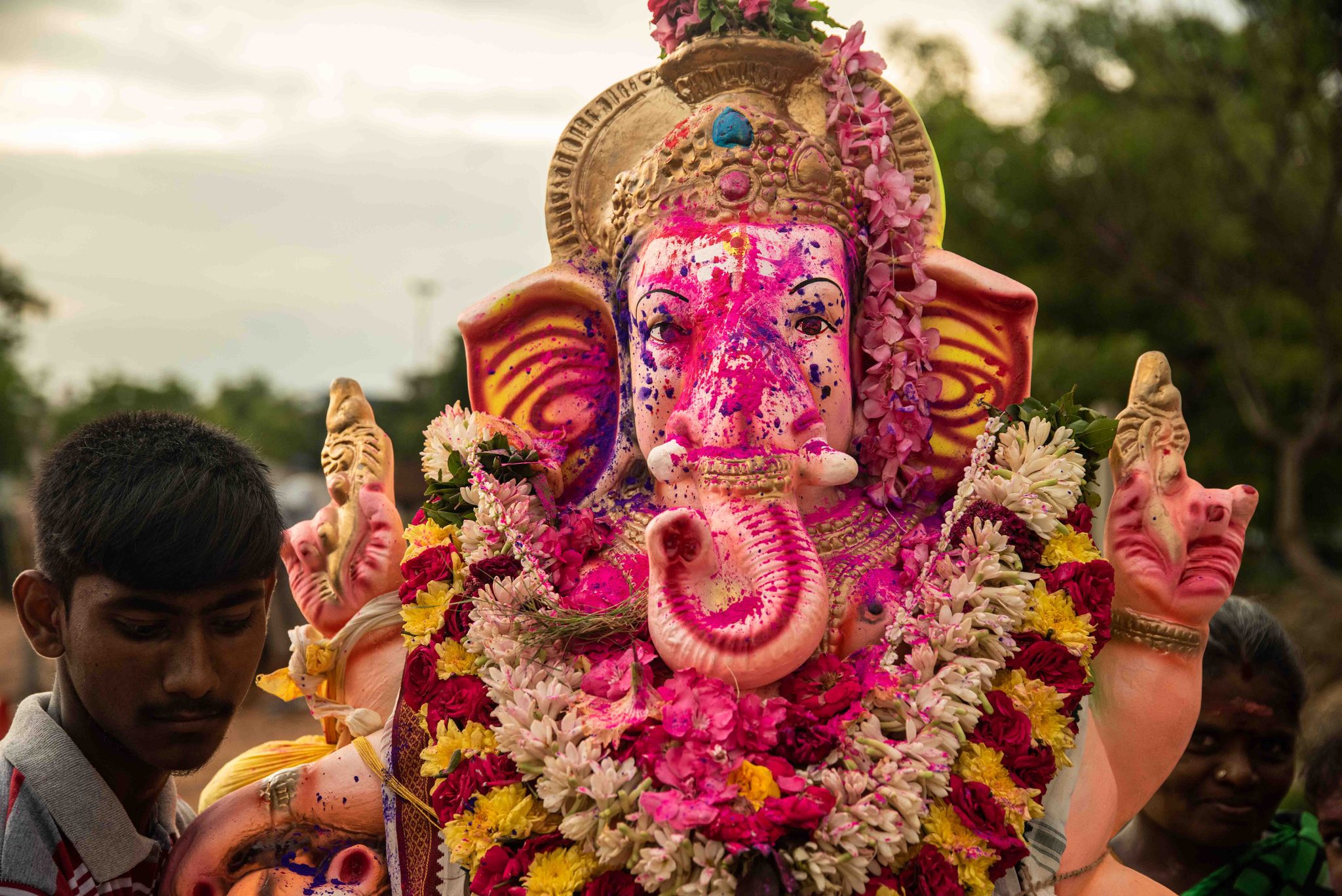Garlanded in flowers, Ganesha waits beside the families who carried him.
