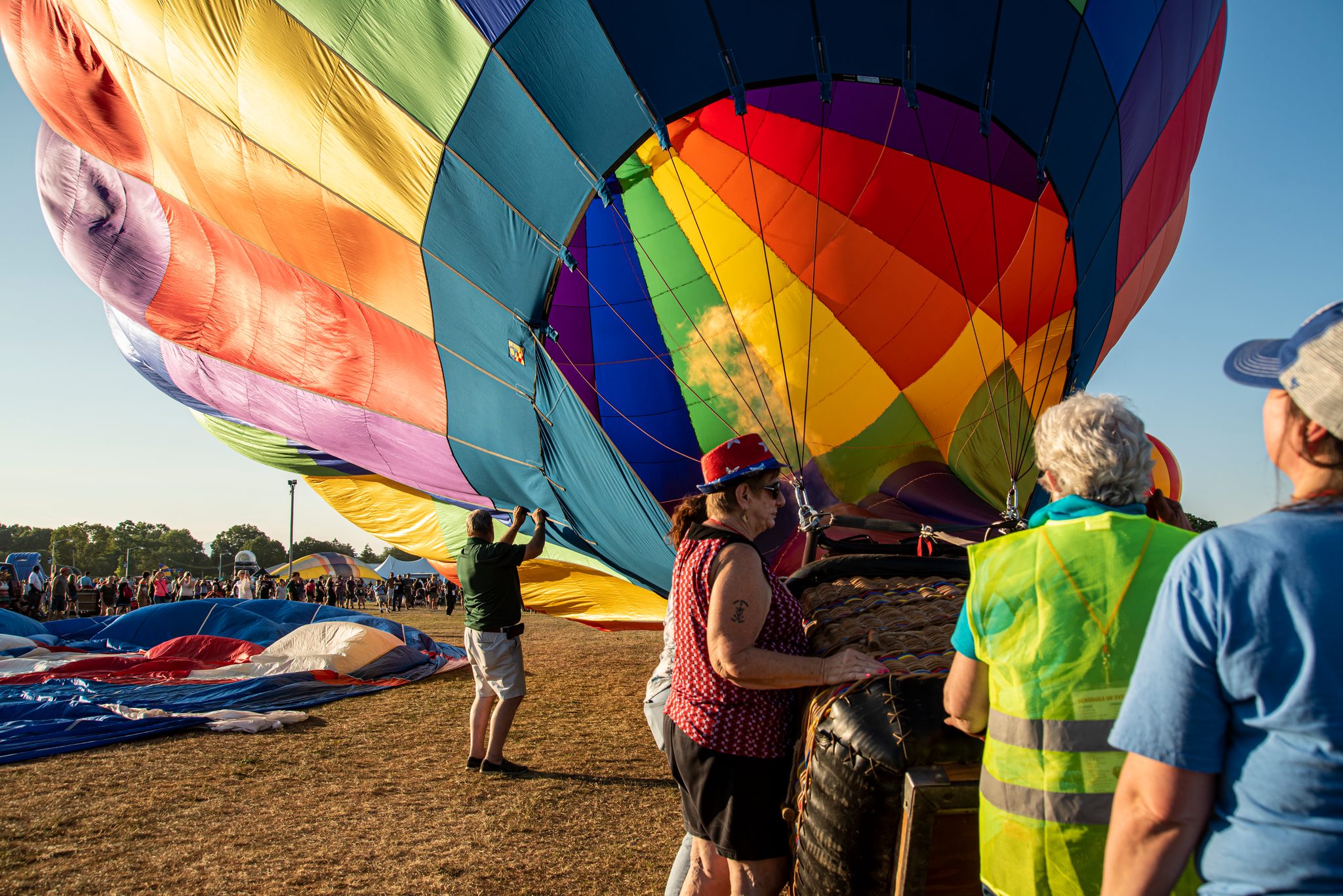 Hands on the ropes, the crew guides a rainbow envelope toward standing.