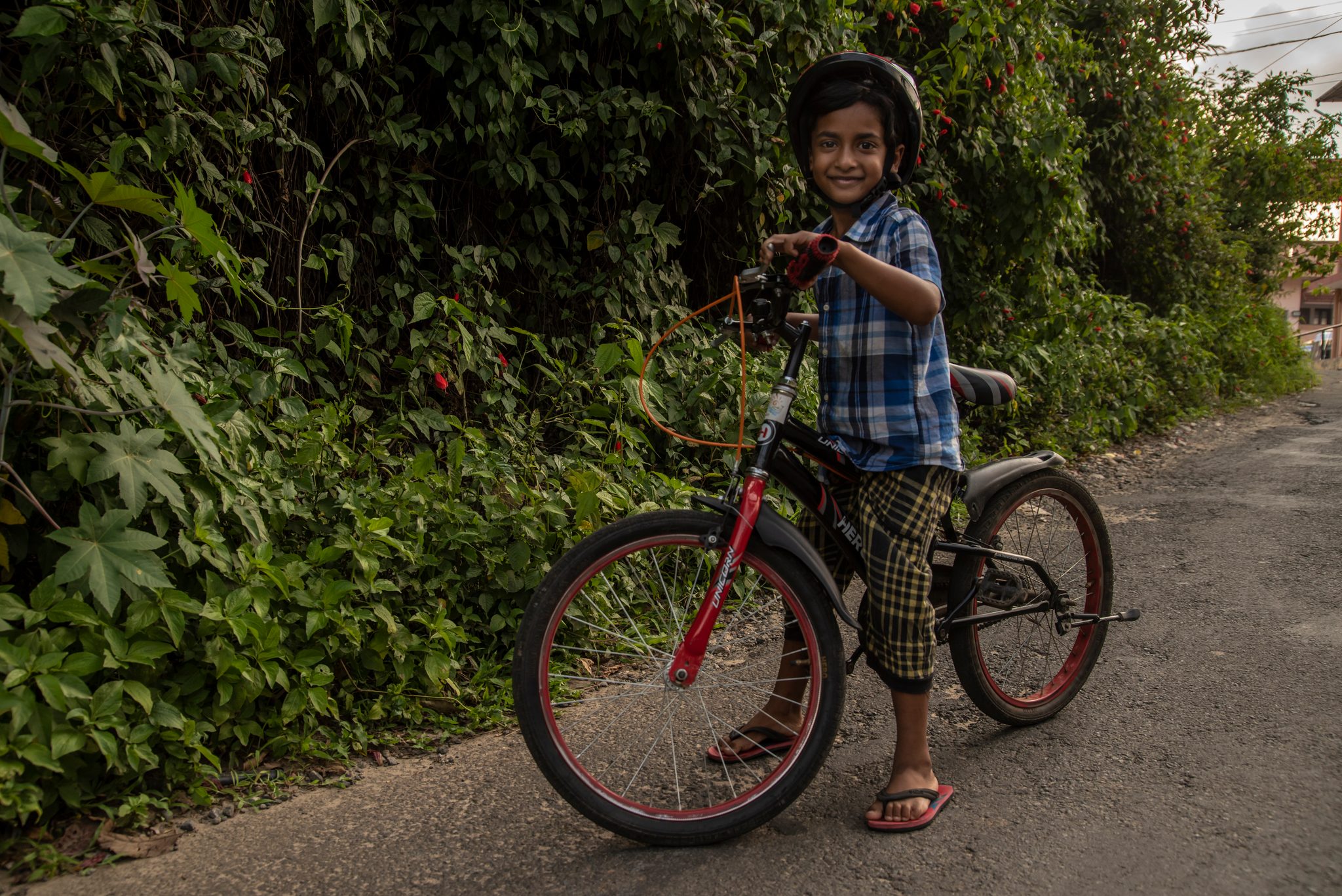 A boy in a helmet grins over his handlebars on a green lane.