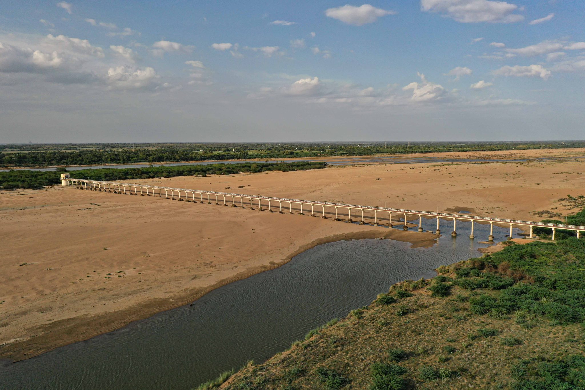 A long bridge crosses a riverbed that is mostly sand, the water a narrow channel below.