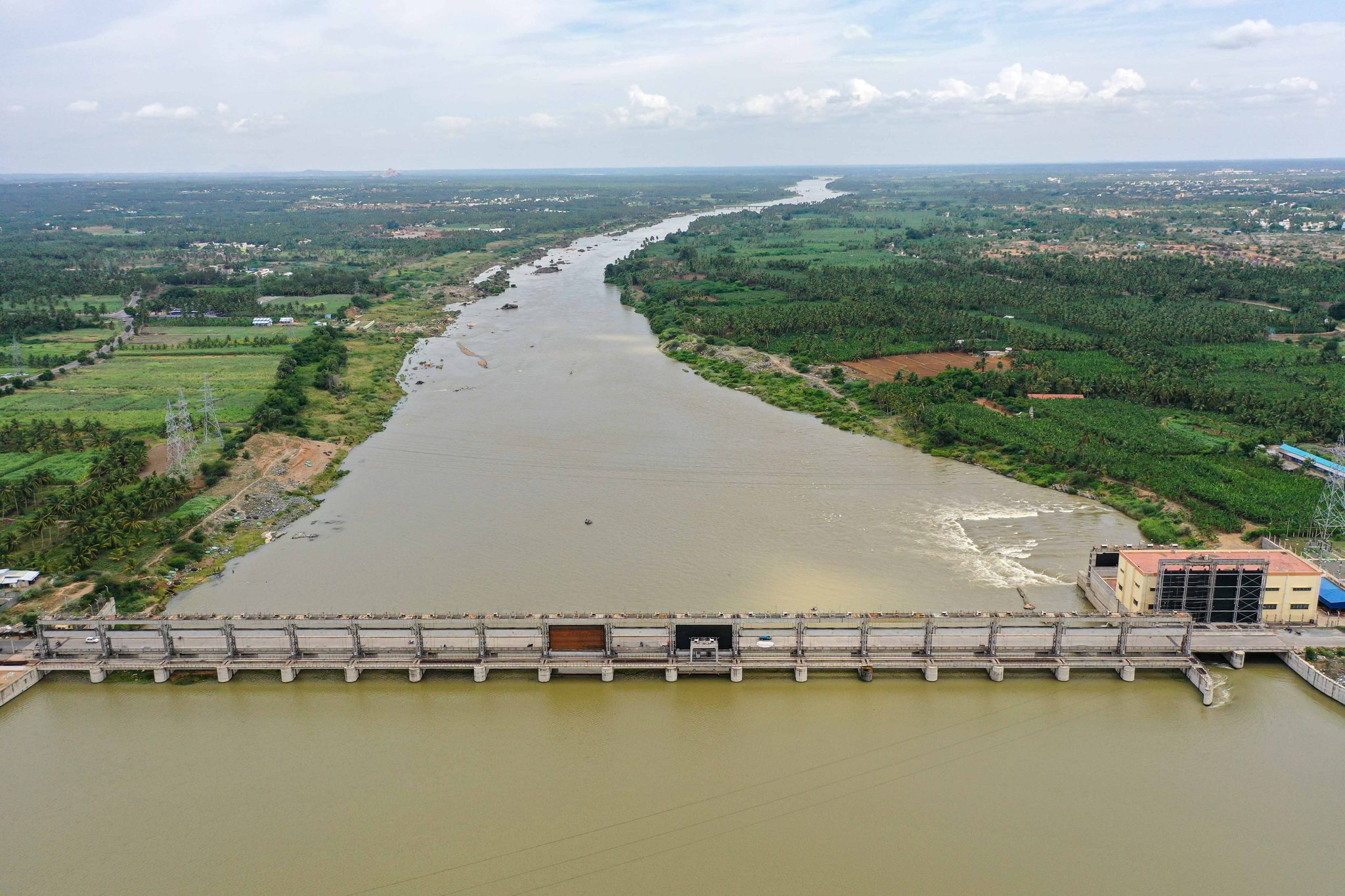 A barrage spans the wide brown river, the farmland stretching away on both banks.