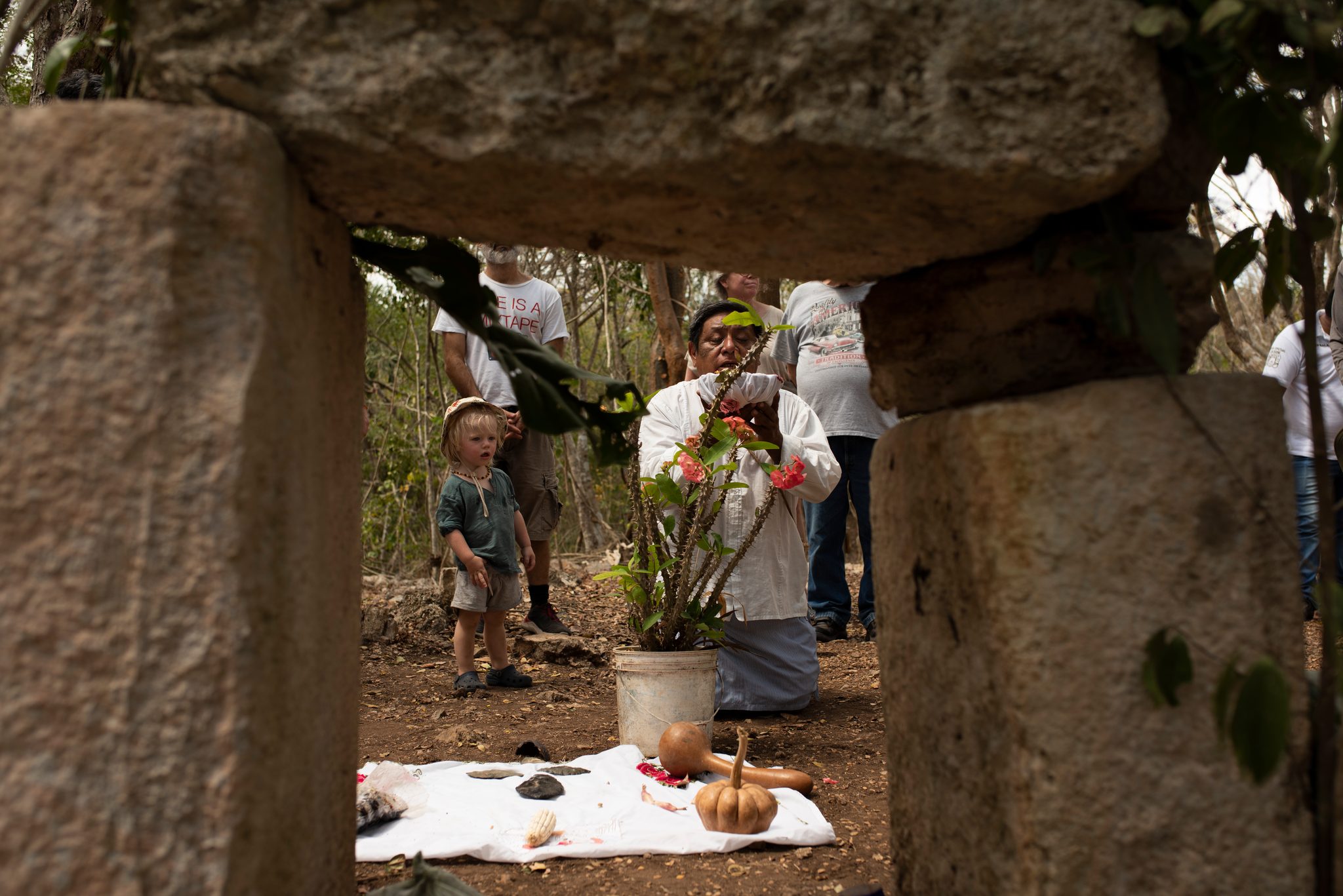 Framed by a stone doorway, the elder kneels at the altar while a child watches.