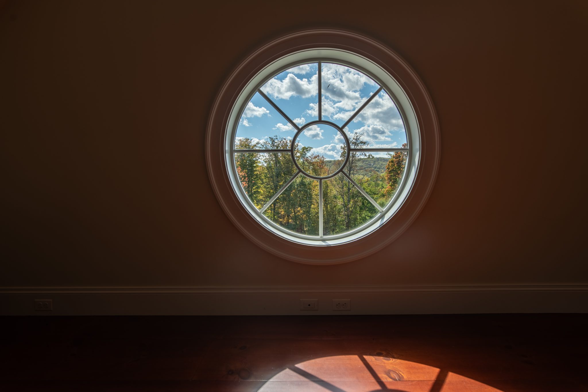 A round window throws a small pool of October sun across a dark wood floor.