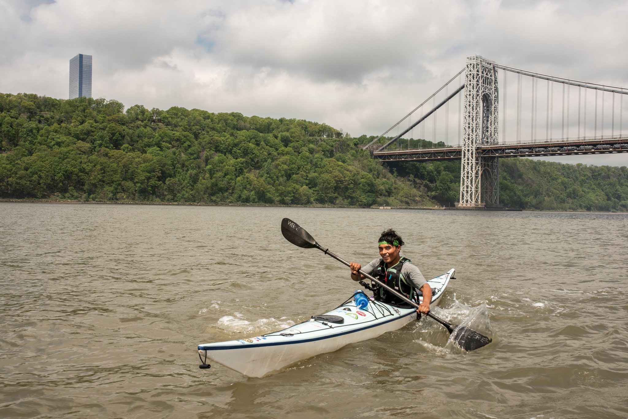 A paddler digs in hard in a white kayak, the bridge and a lone tower standing over his shoulder.