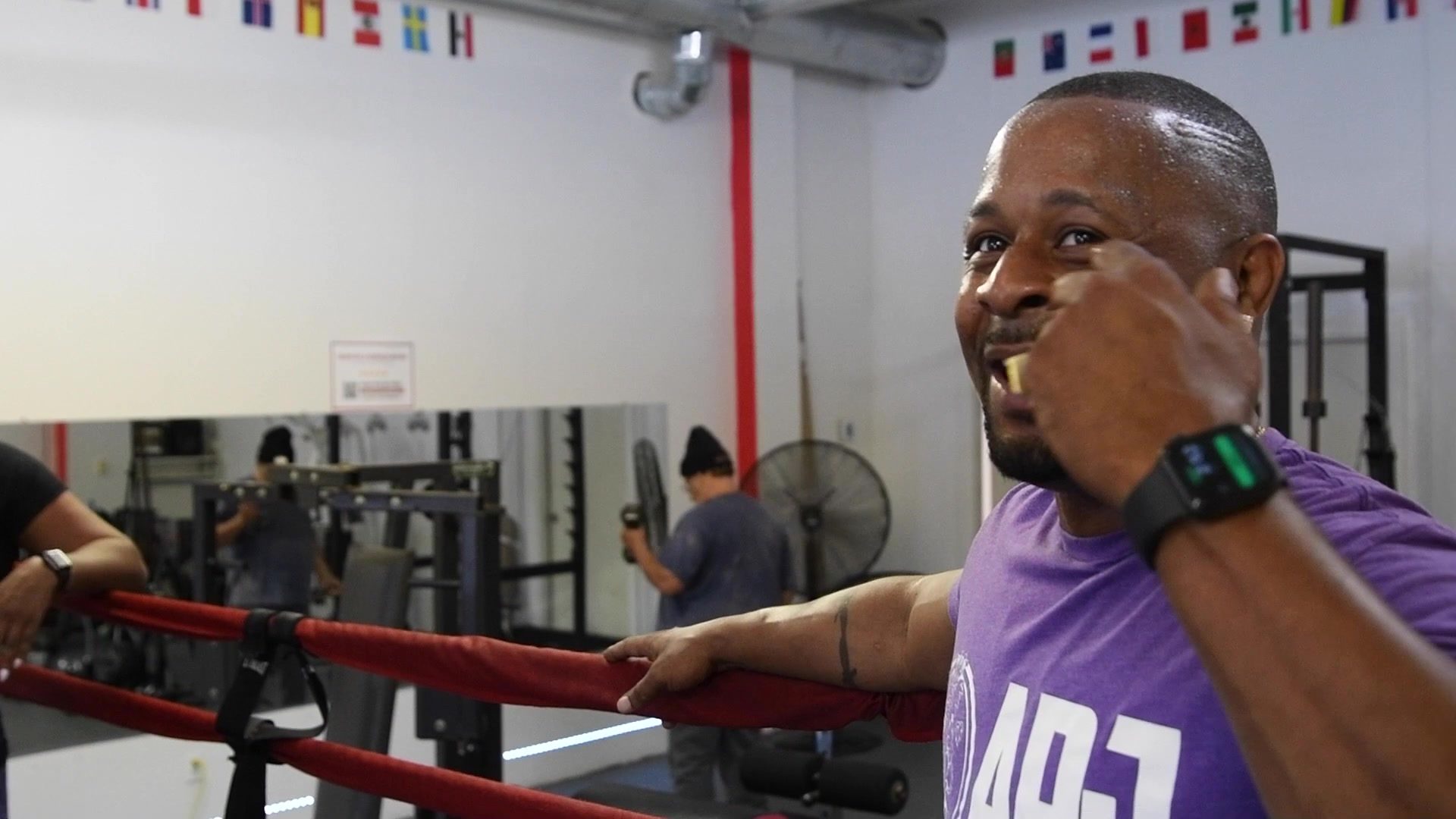 At the ropes in a purple club shirt, Coach Kariym throws a mock punch at the camera and laughs.