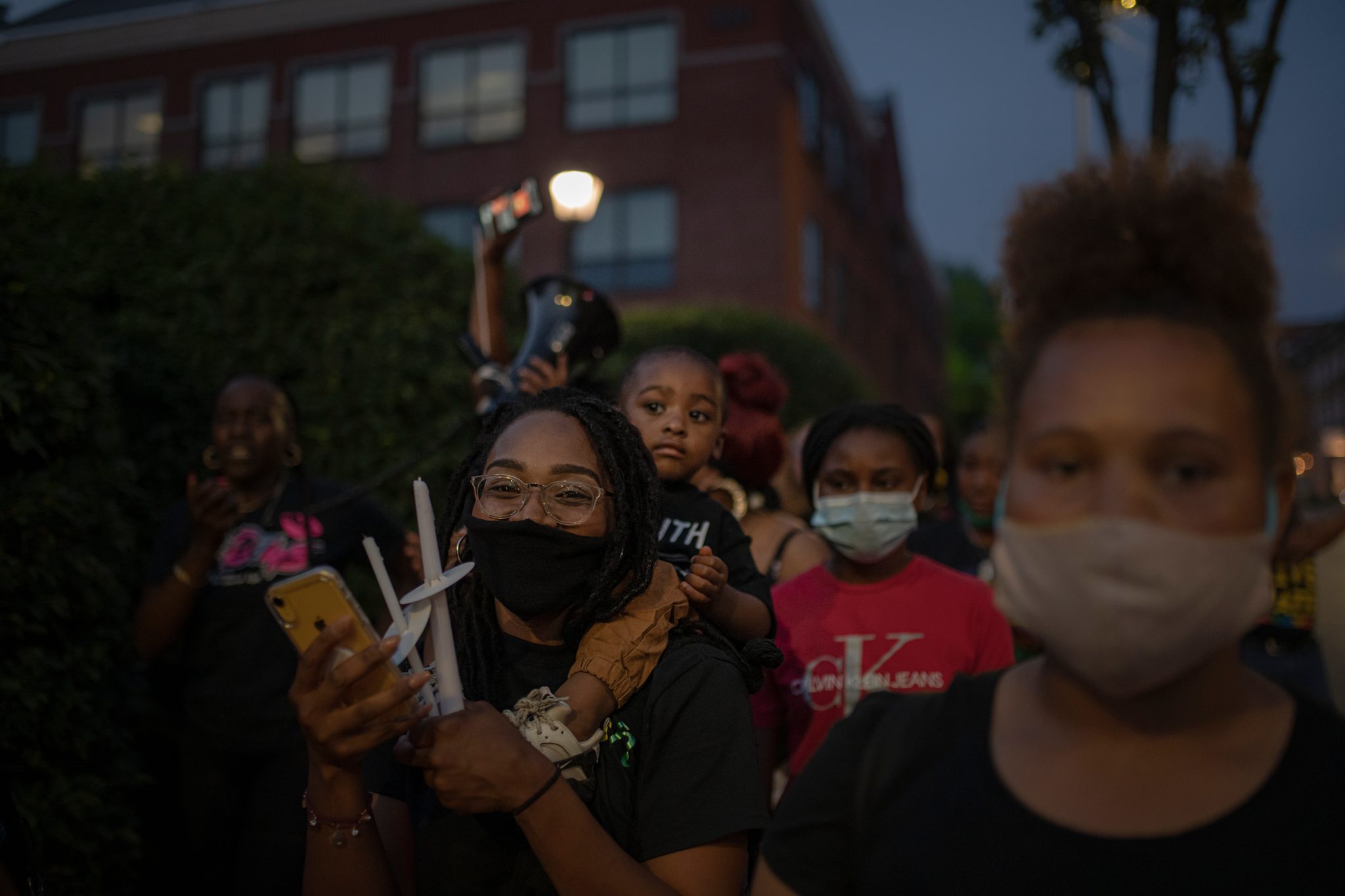 Women and children gather with candles, a little one riding high on someone's shoulders.
