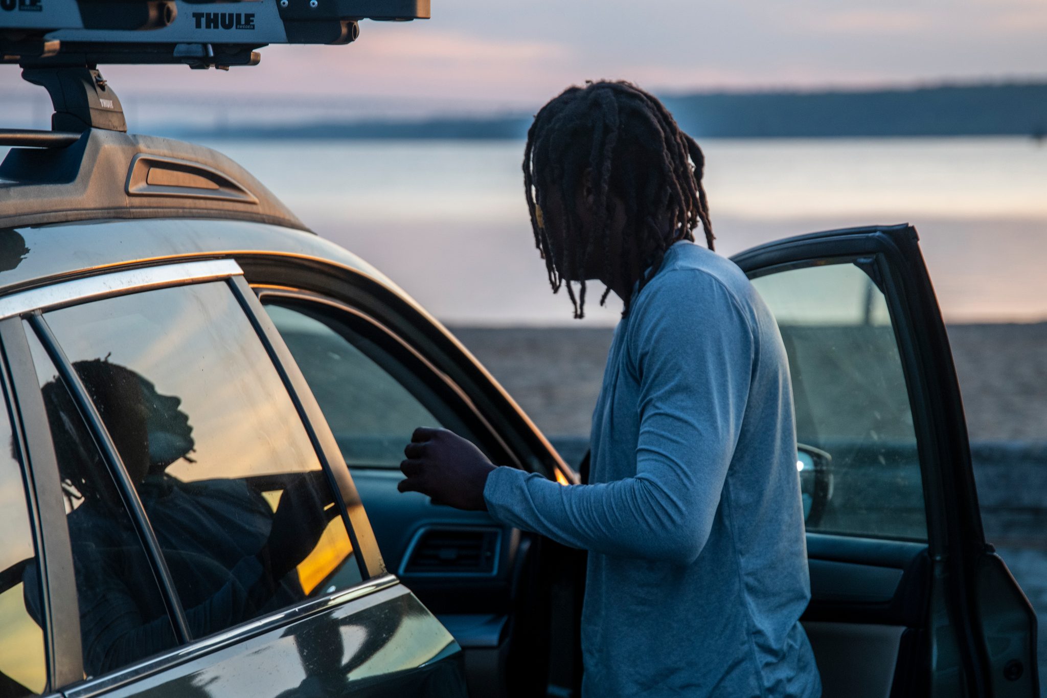 Before sunrise, Chev leans into the open car door, the river already pink behind the lot.