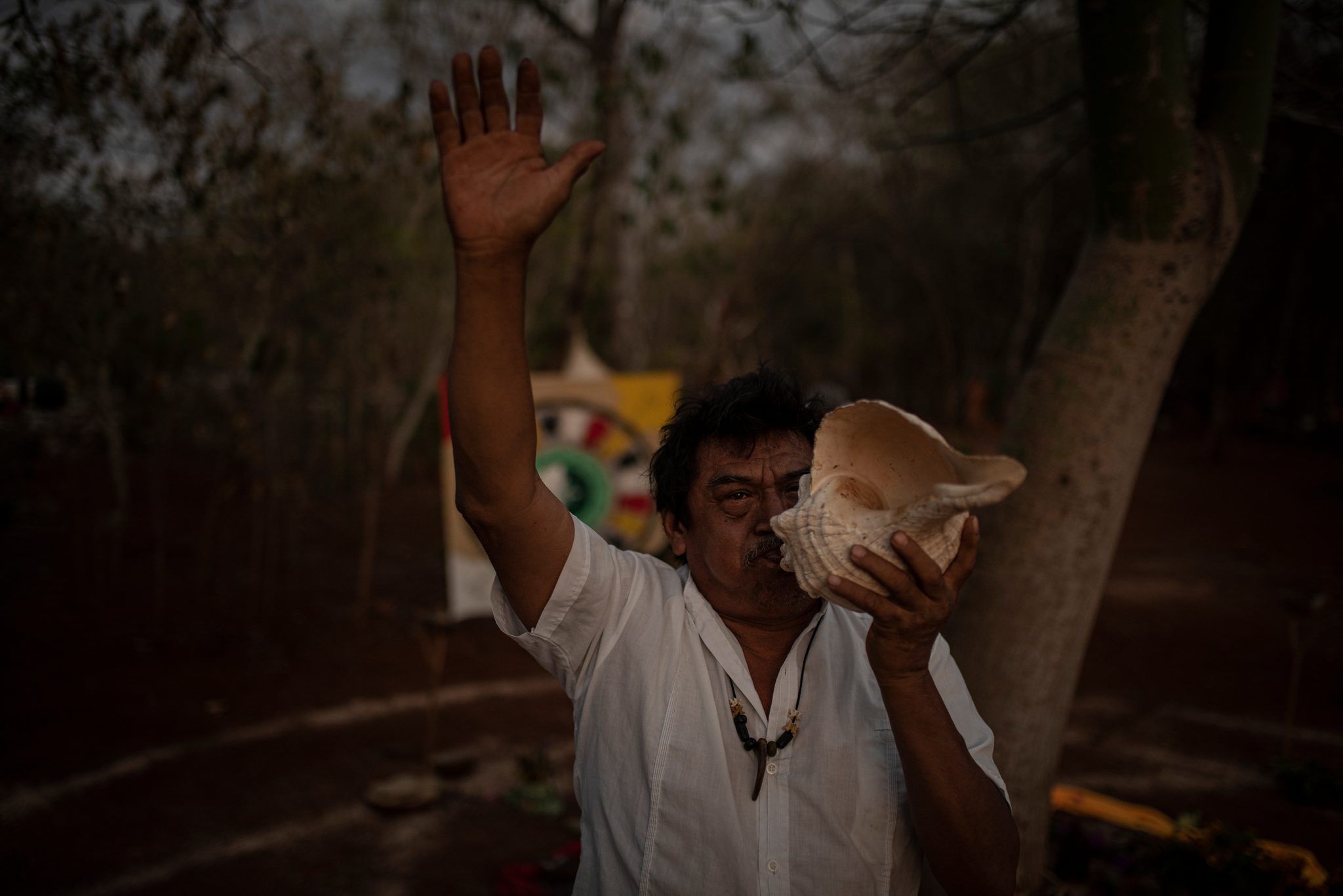 A man raises one hand to the sky and sounds the conch shell.