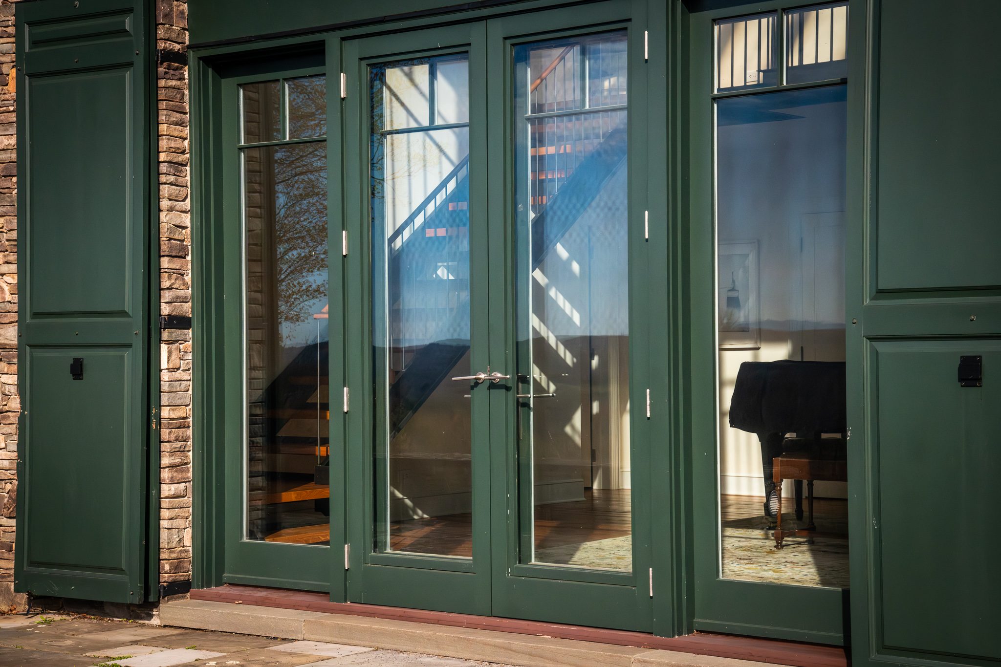 Green-painted French doors set deep in a fieldstone wall, with a piano just visible in the April room beyond.