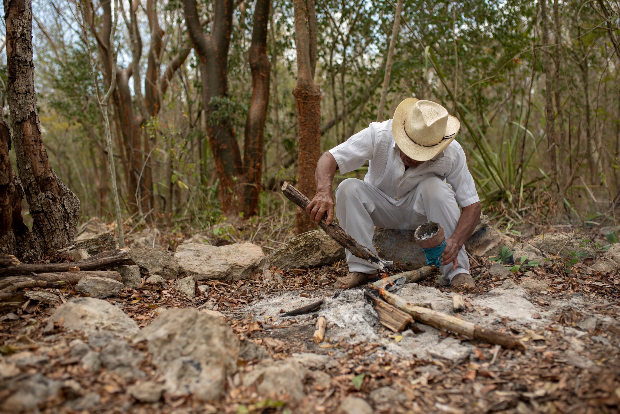 He crouches to tend the fire before the ceremony begins.