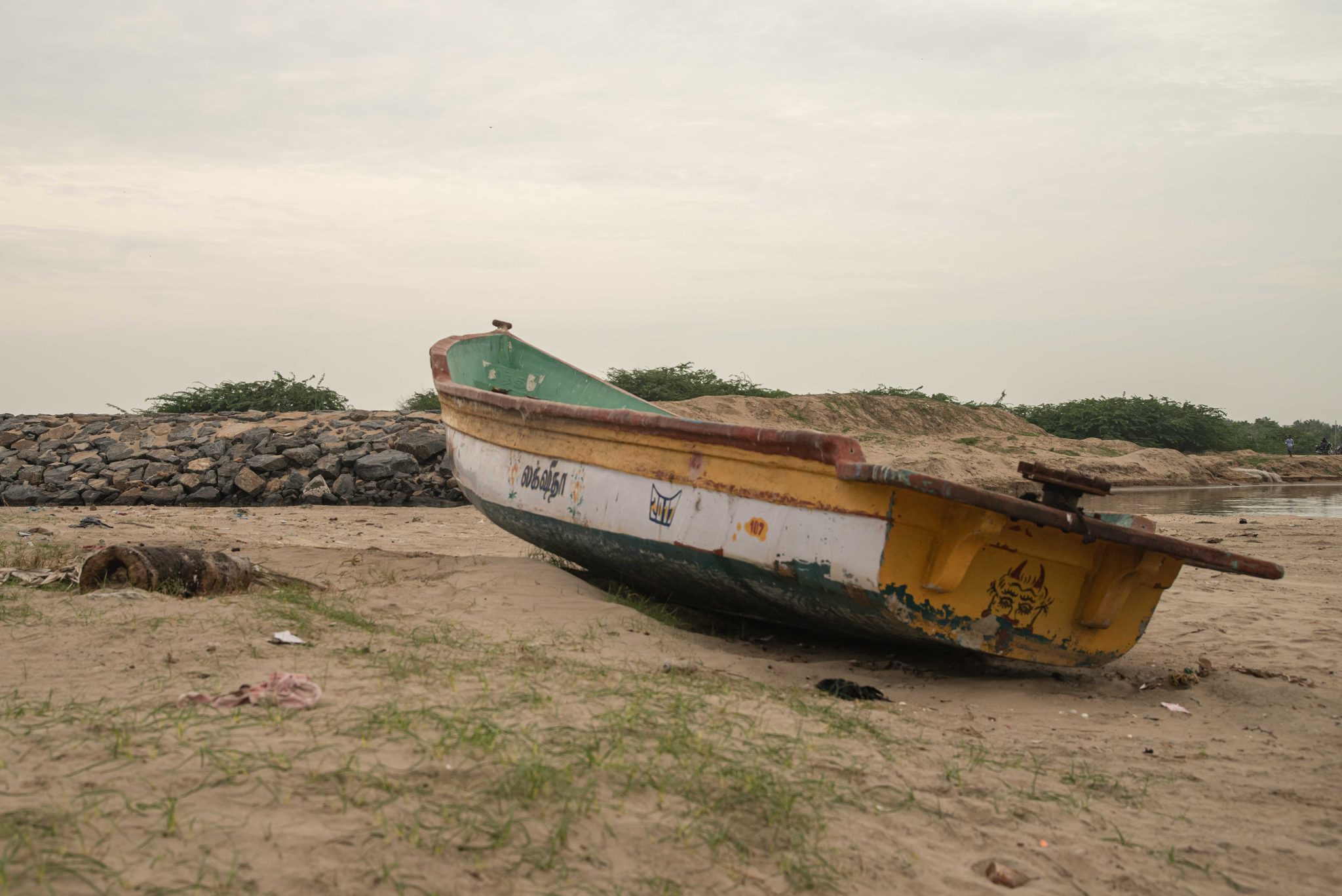 A yellow and white boat leans on the sand beside the rocks.