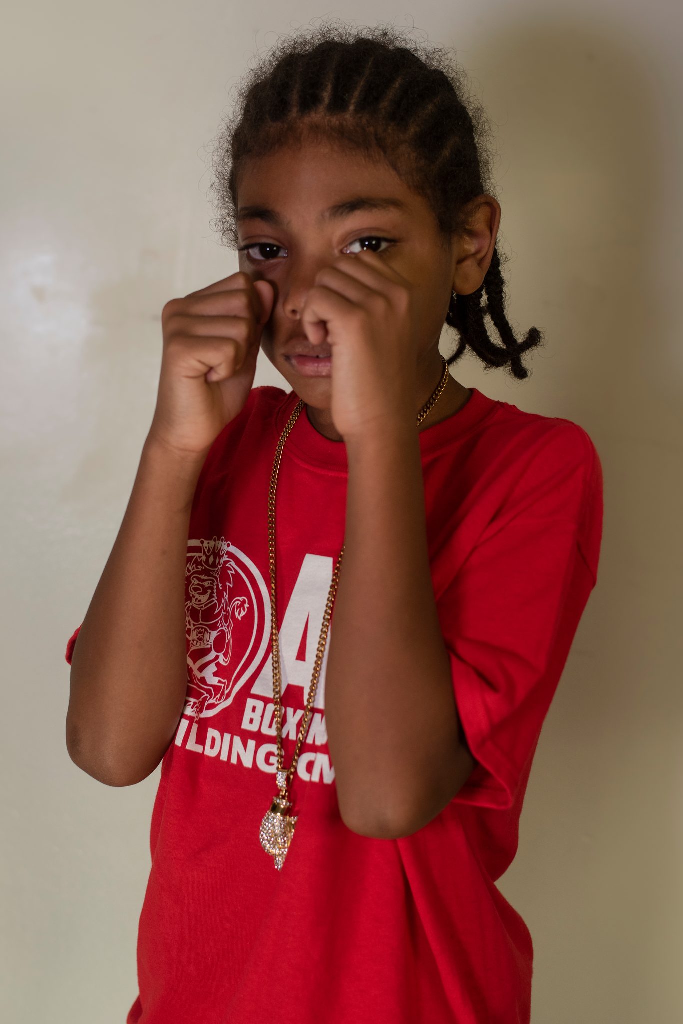 Cornrows pulled back and fists at her eyes, a young boxer peers out from behind her guard.