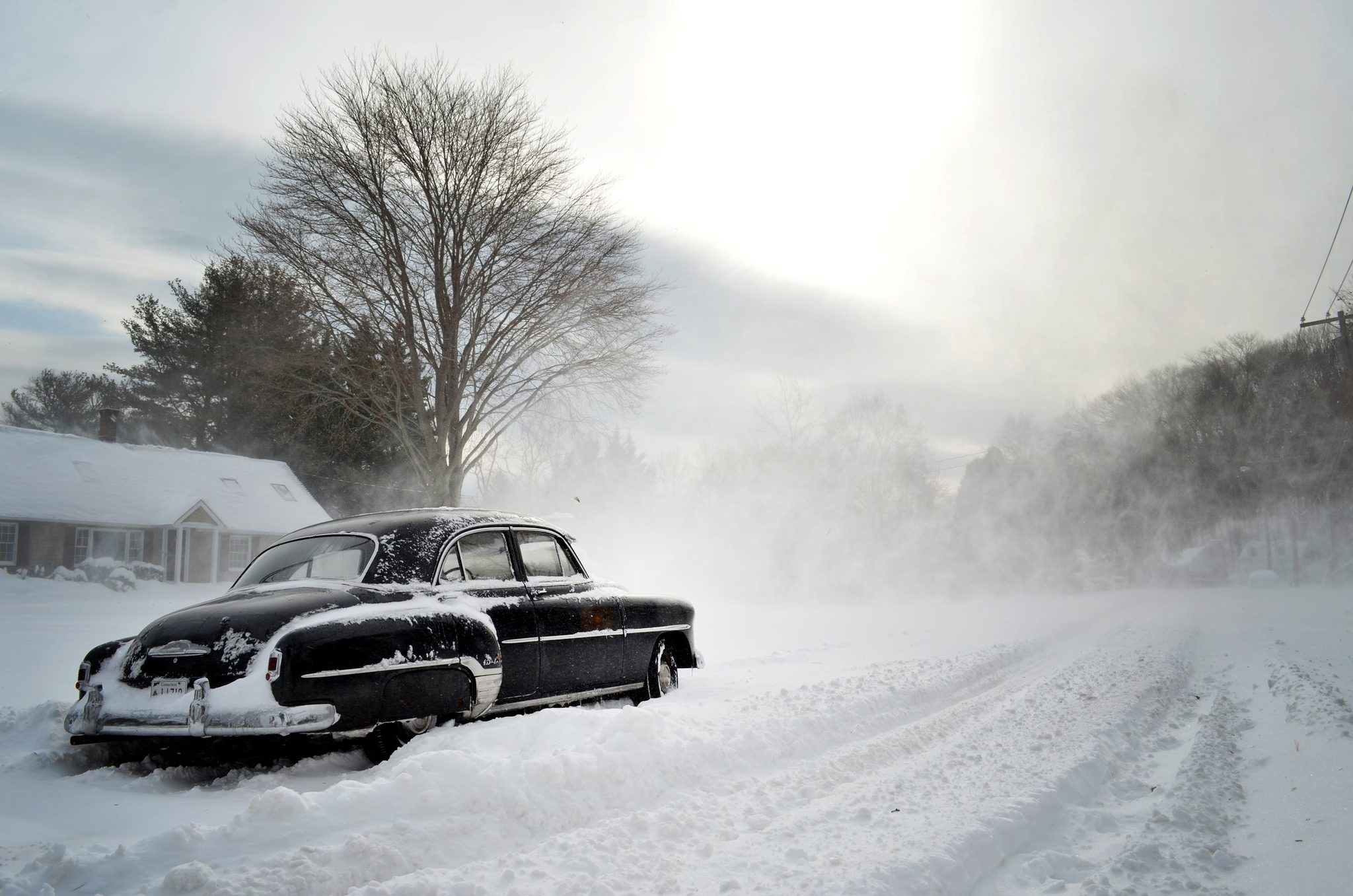 An old sedan sleeps under drifting snow, its chrome the only thing the storm hasn't claimed.
