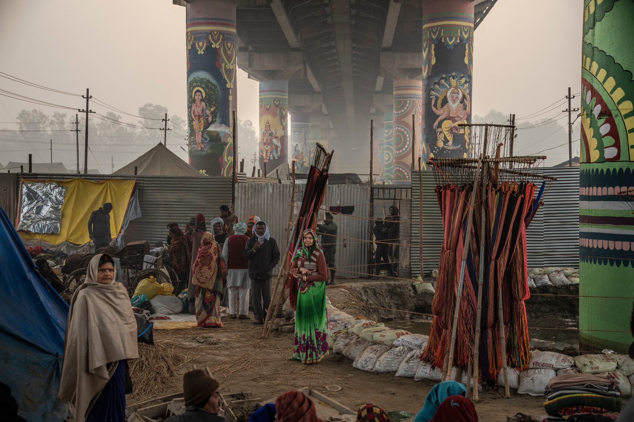 People gather beneath a painted cement bridge within the Mela.