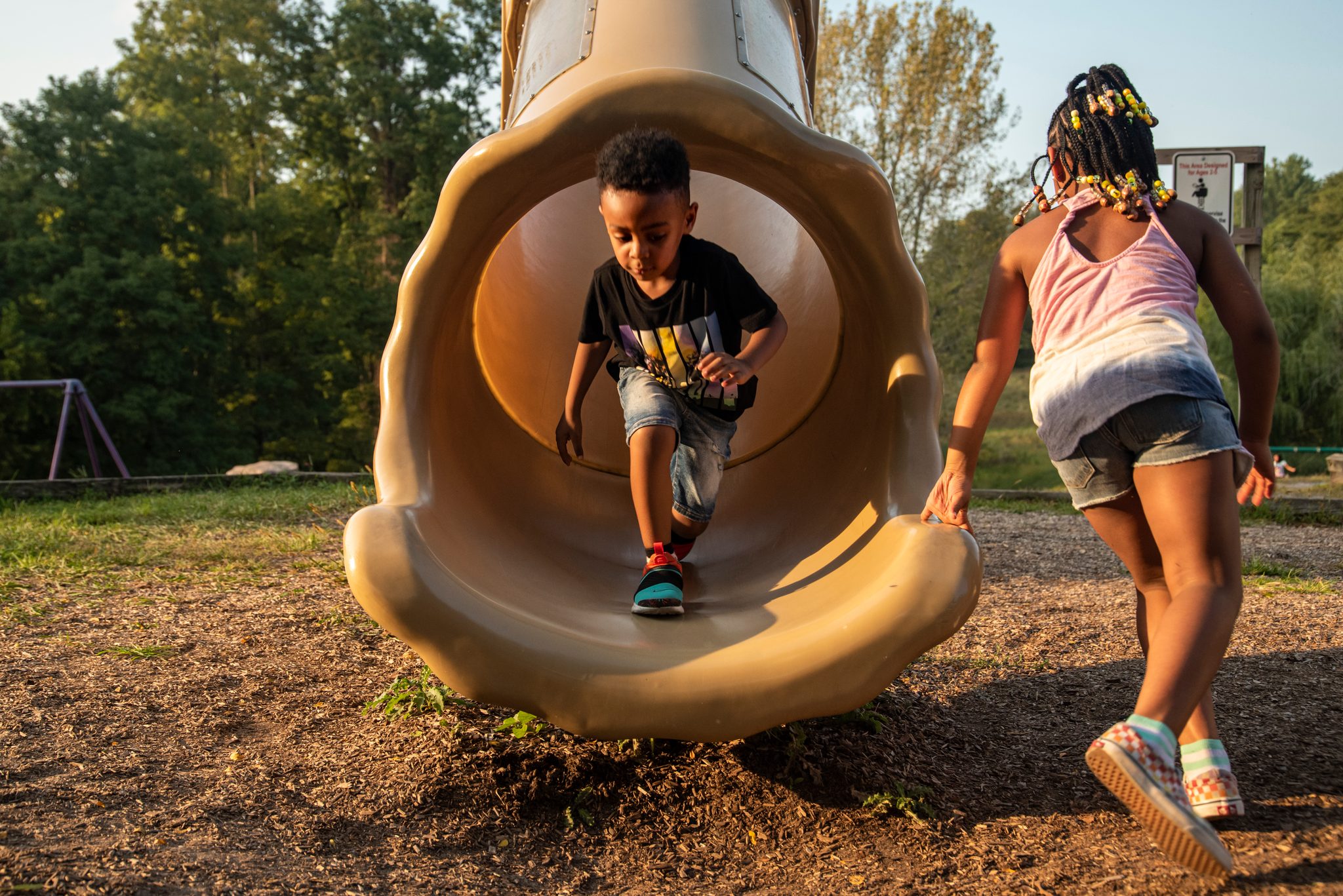 A boy shoots out of the tube slide while his friend races around for another turn.