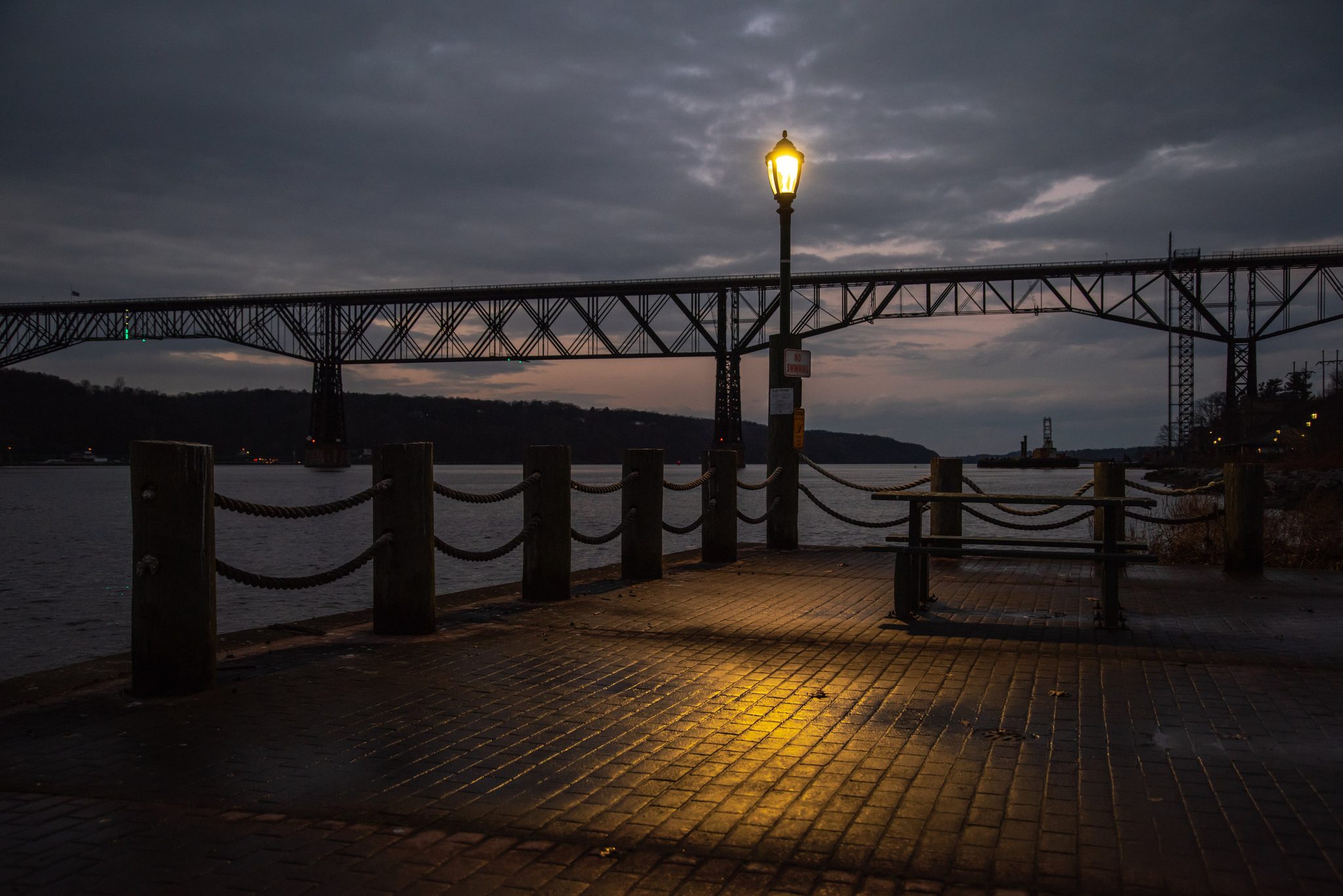 A lamp glows on the empty pier, the old railroad bridge across the river. We wearisome beasts, fumbling feet racing towards dusk.