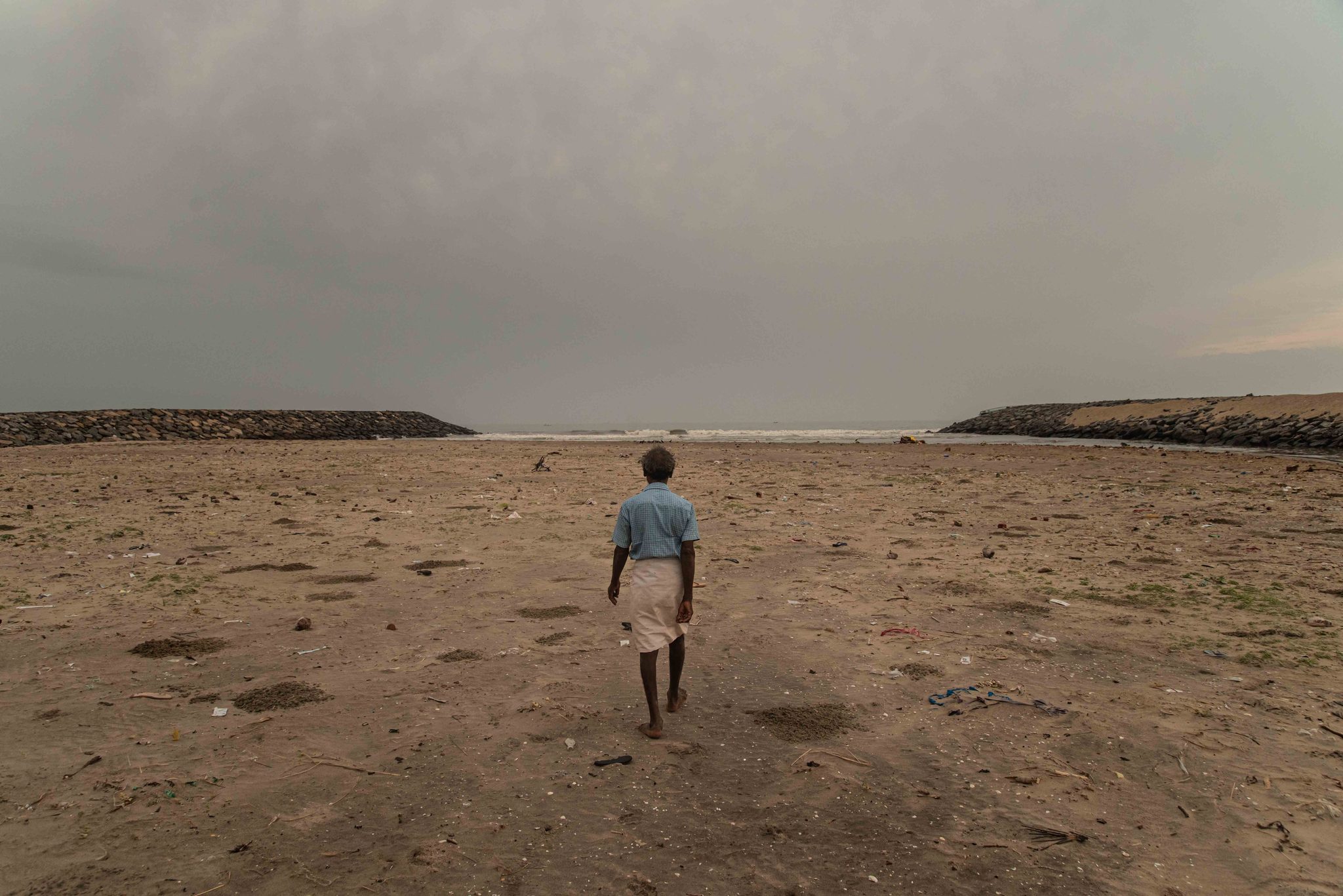 A man walks toward the sea between the breakwaters at the river's mouth.