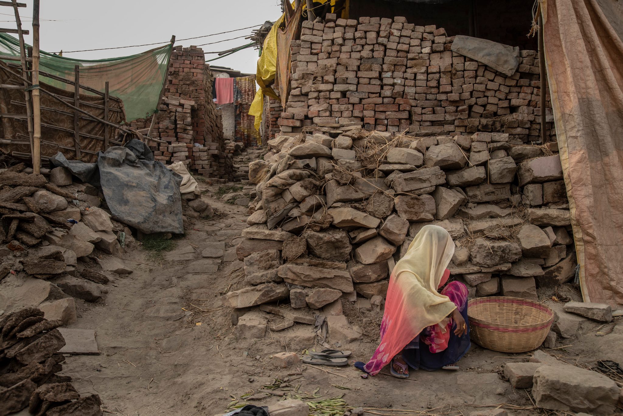 On the outskirts of the Mela, a woman sits among piled bricks with her basket.