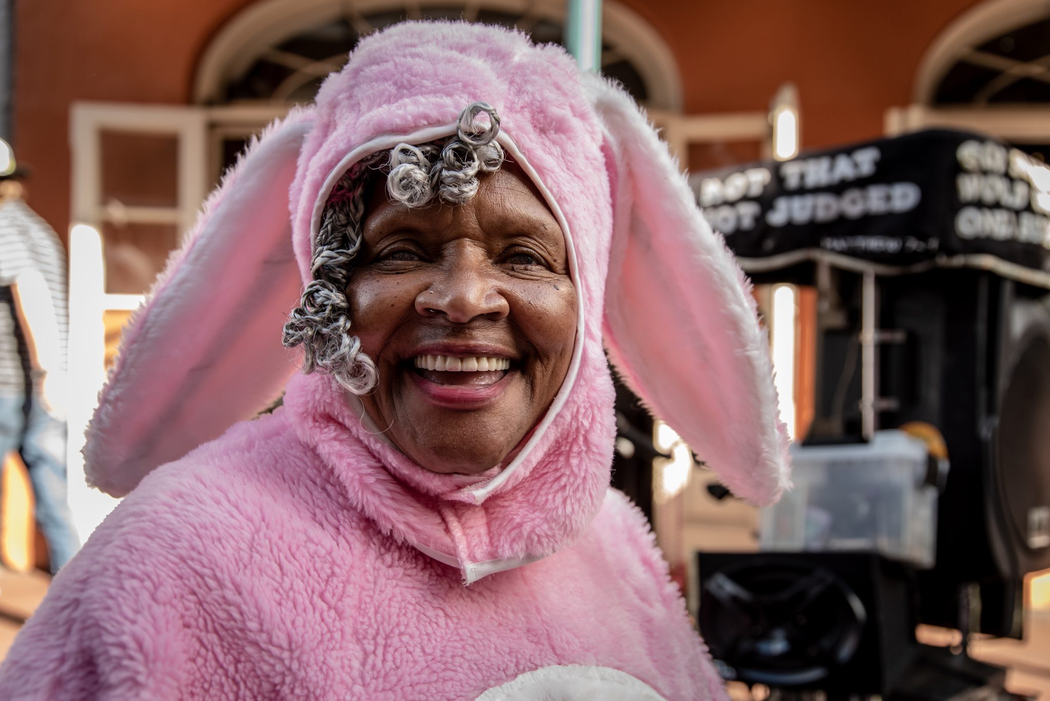 A woman in a pink bunny suit beams at the camera, curlers peeking out.