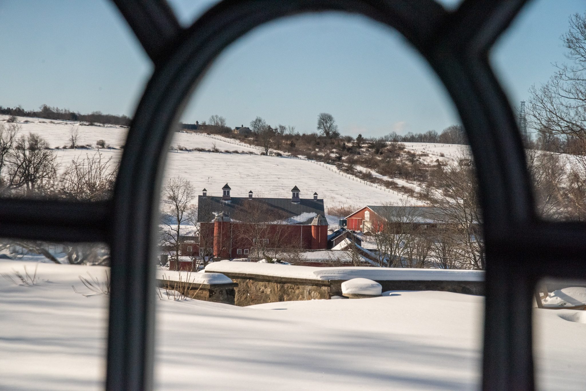 Through an arched window, the red barns and white hills beyond.