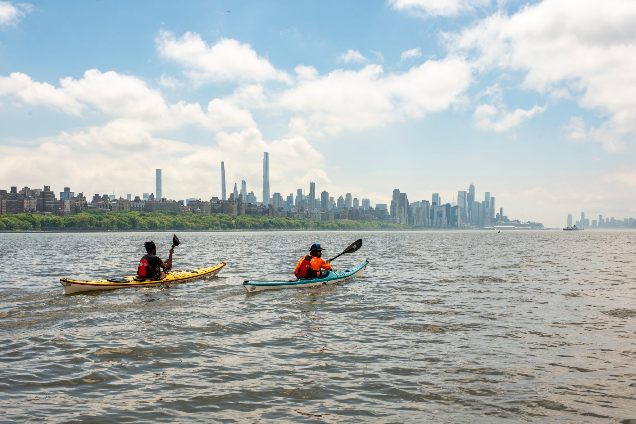 Clouds break open over the river and the Midtown skyline lines up on the horizon ahead of two boats.