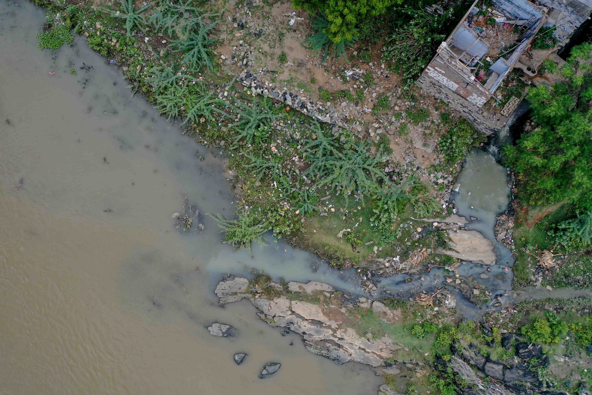 Straight down, a drain spills into the river beside a crumbling house.