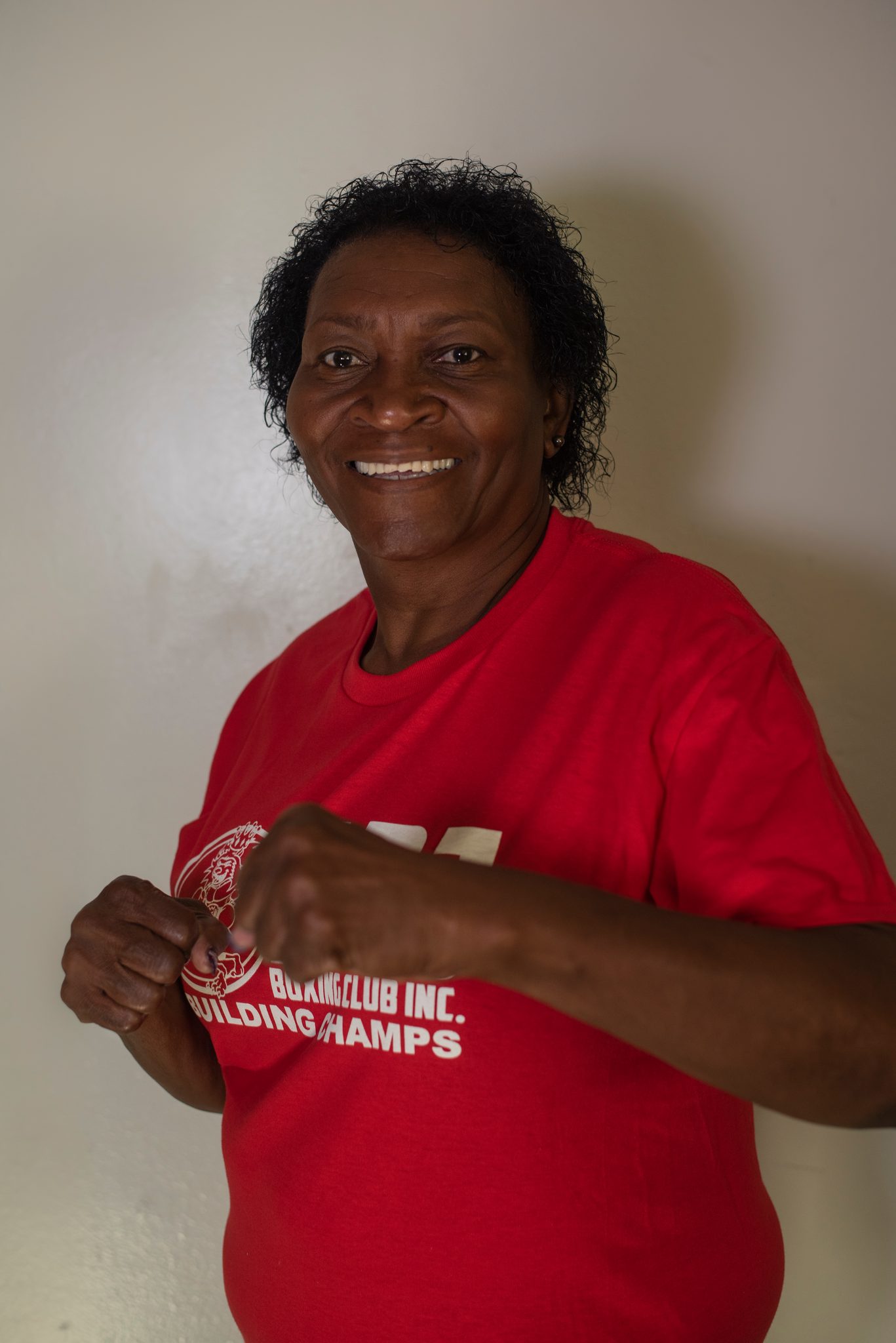 She turns a shoulder toward the lens and curls her fists in front of the logo, still smiling.