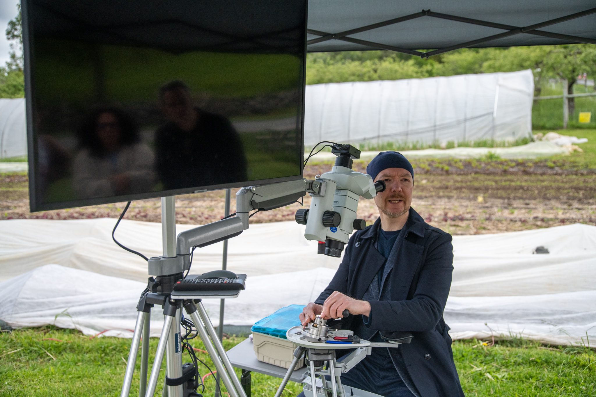 An artist bends to the microscope, the work on the screen beside him.