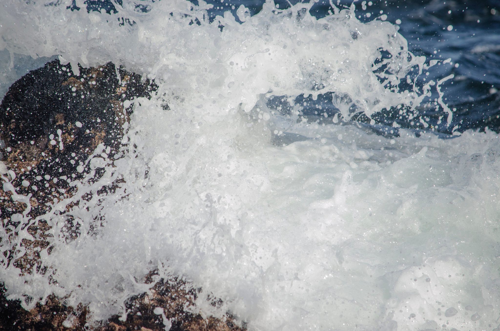A wave explodes over the dark rocks in a burst of white. For even mountains will move when the streams demand it.