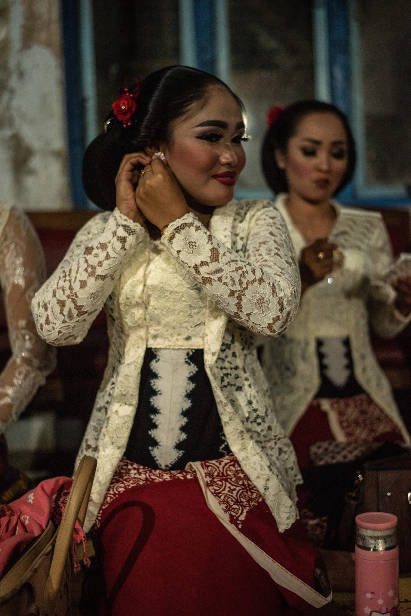 One singer fixes her earring, another checks her face, both in white lace.