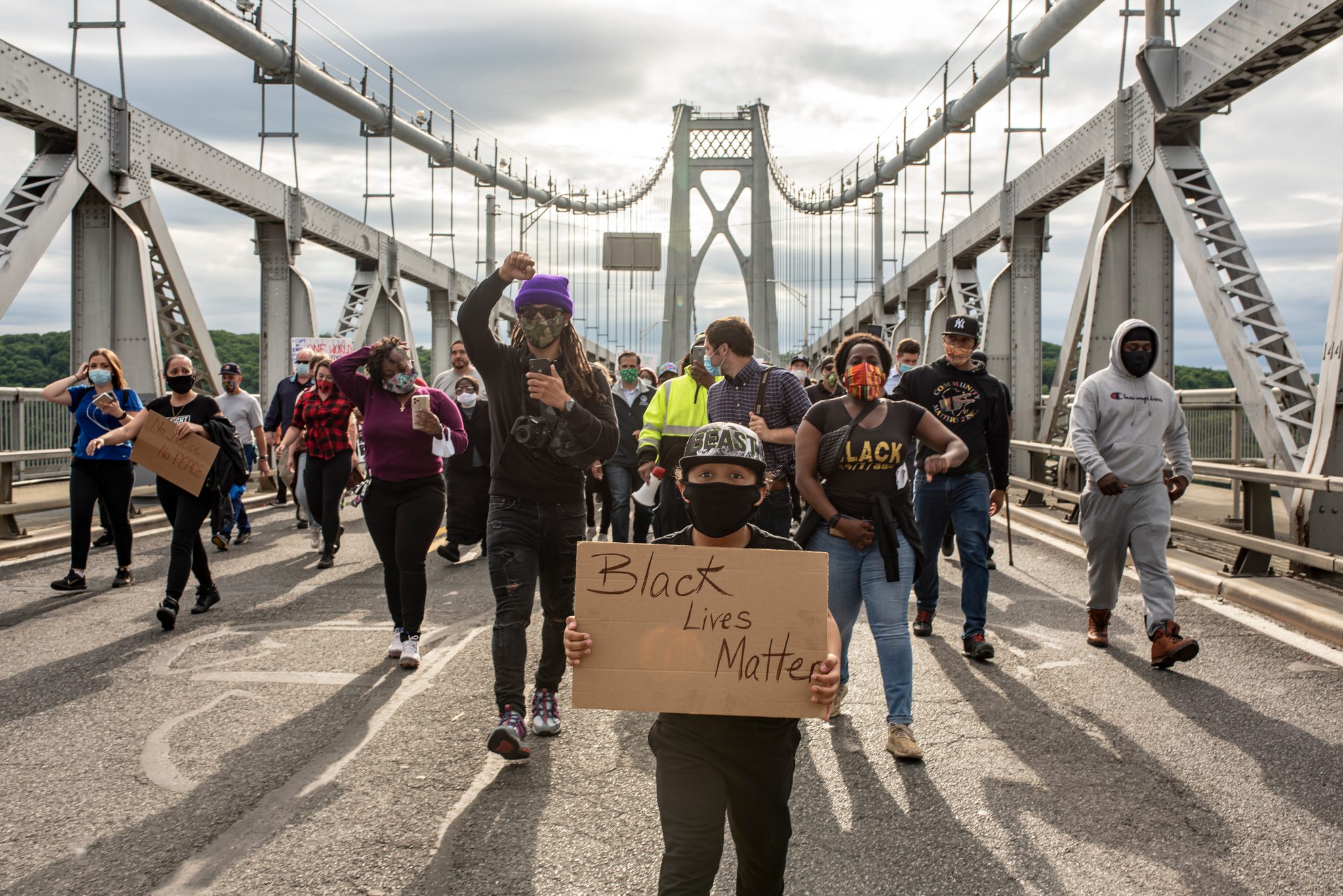 The march crosses the bridge behind a young marcher holding a cardboard sign.