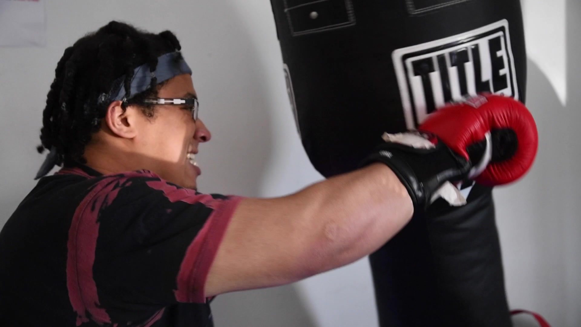 Red gloves drive into a heavy bag, glasses and a headband holding steady through the punch.