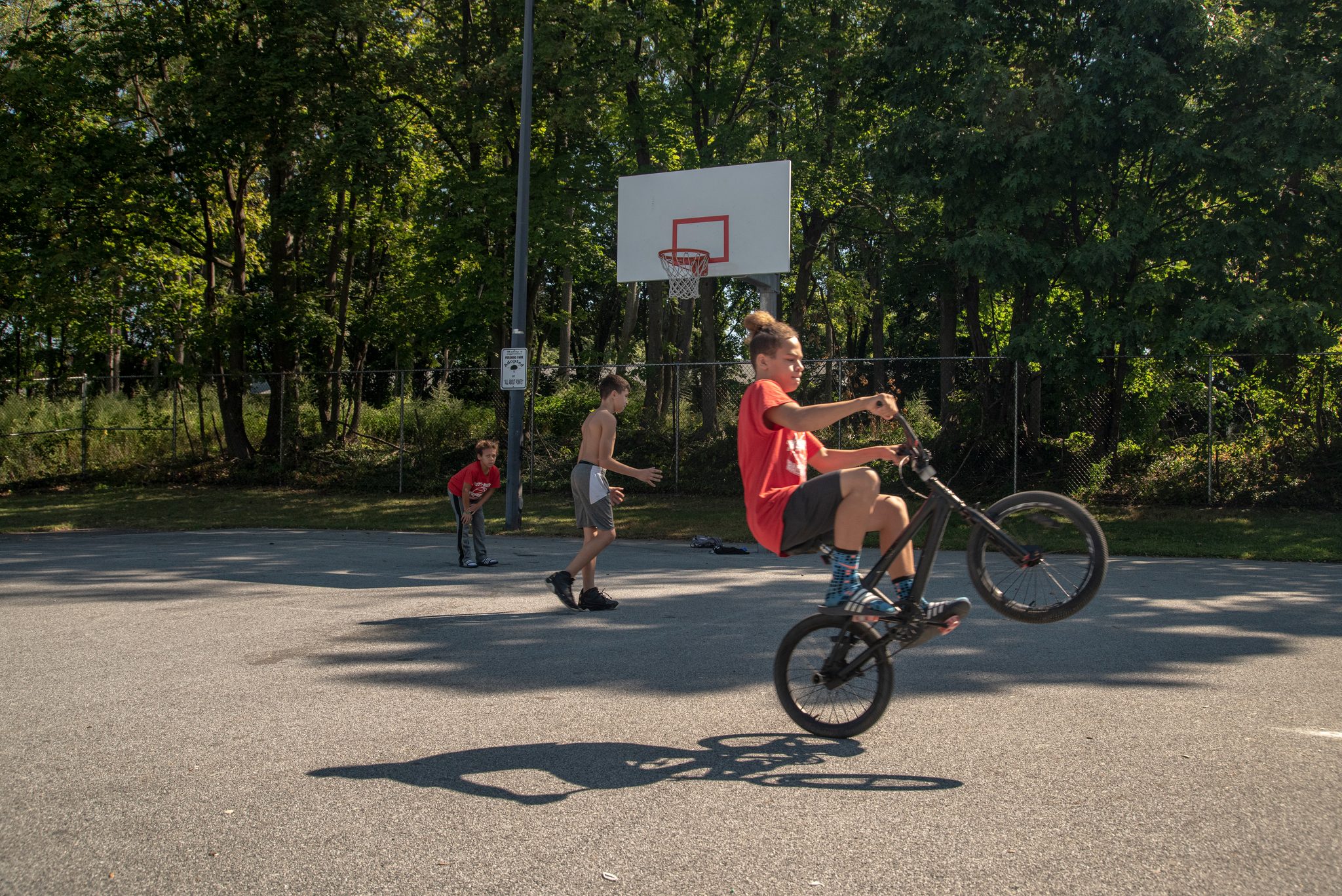 A boy pops a wheelie across the basketball court while his friends shoot around.