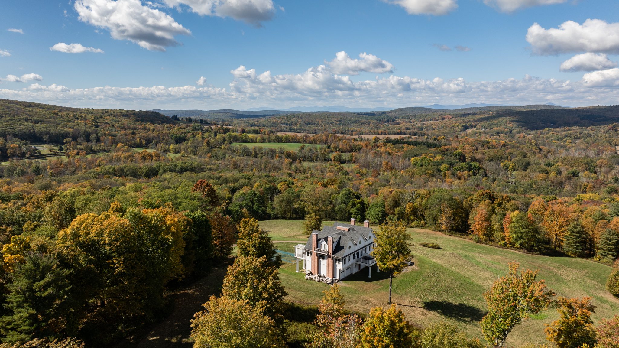 Early October color rolls across the hills around a white farmhouse set high on its open meadow.