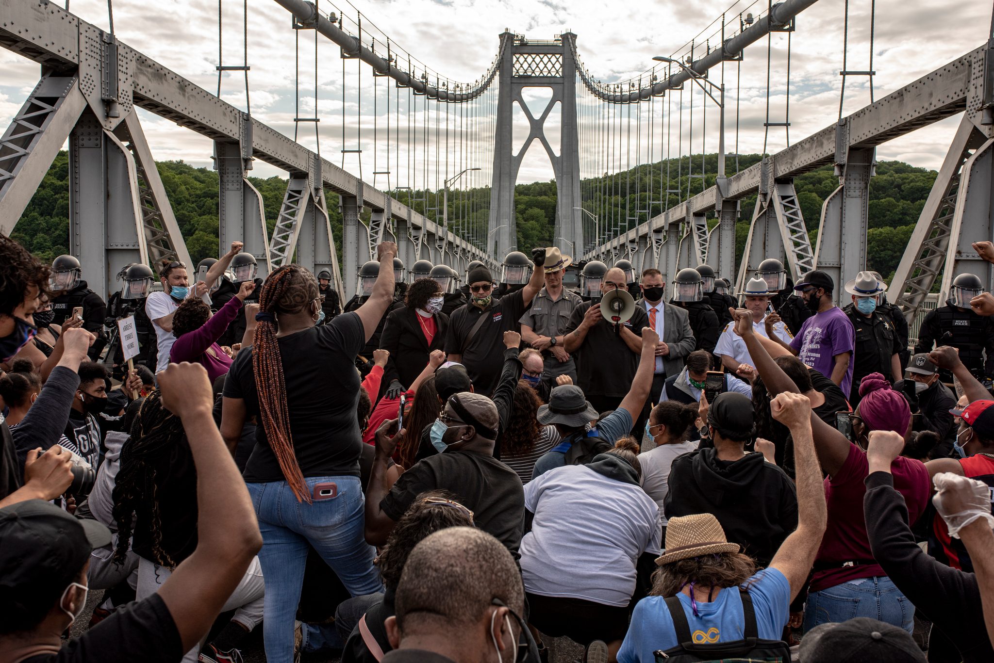 Marchers sit down on the bridge deck in front of the line, fists in the air.