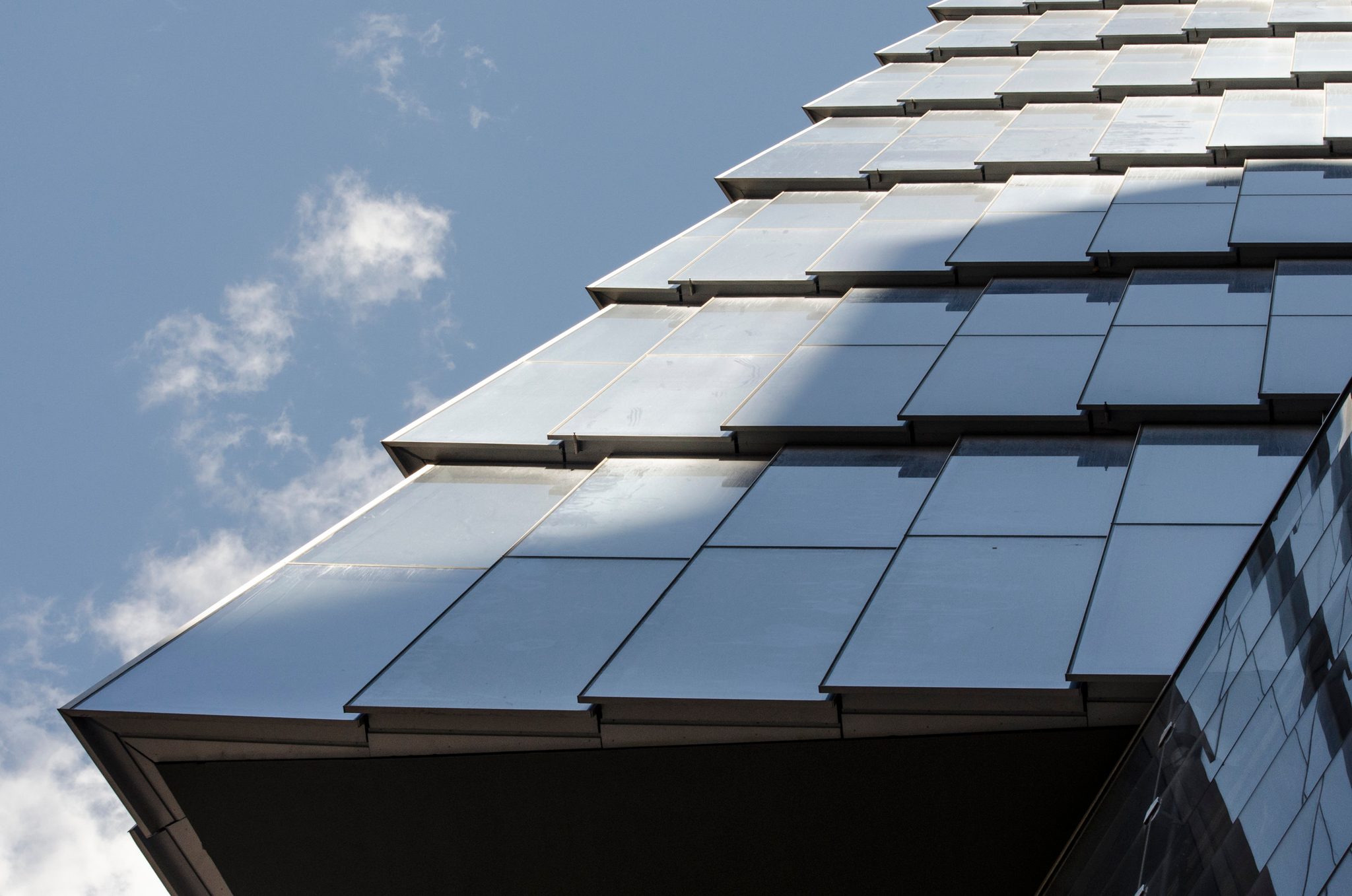 Glass shingles step up the side of a building, catching the clouds.