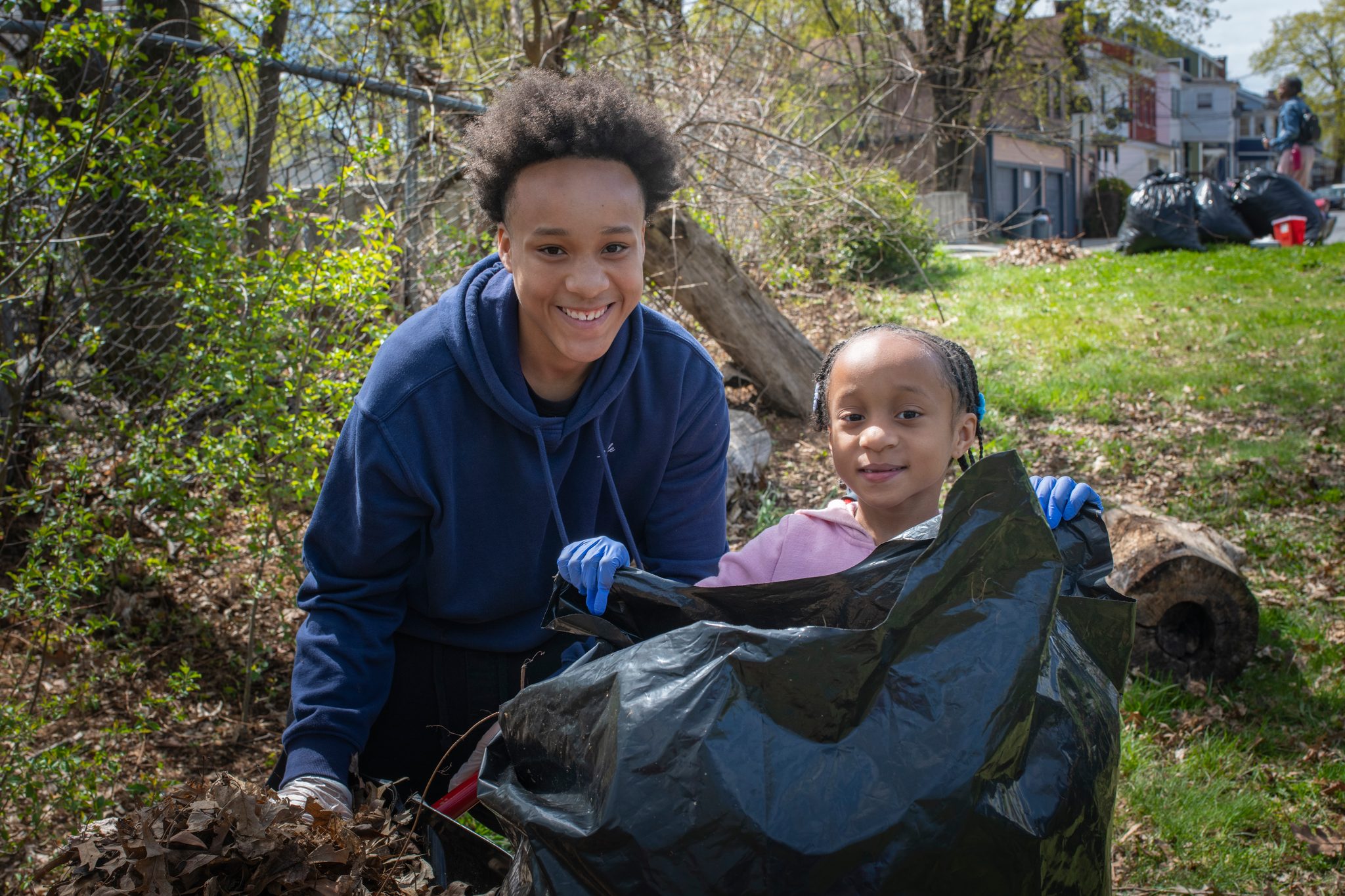 A teenager holds the bag open while a small helper drops in what she found.
