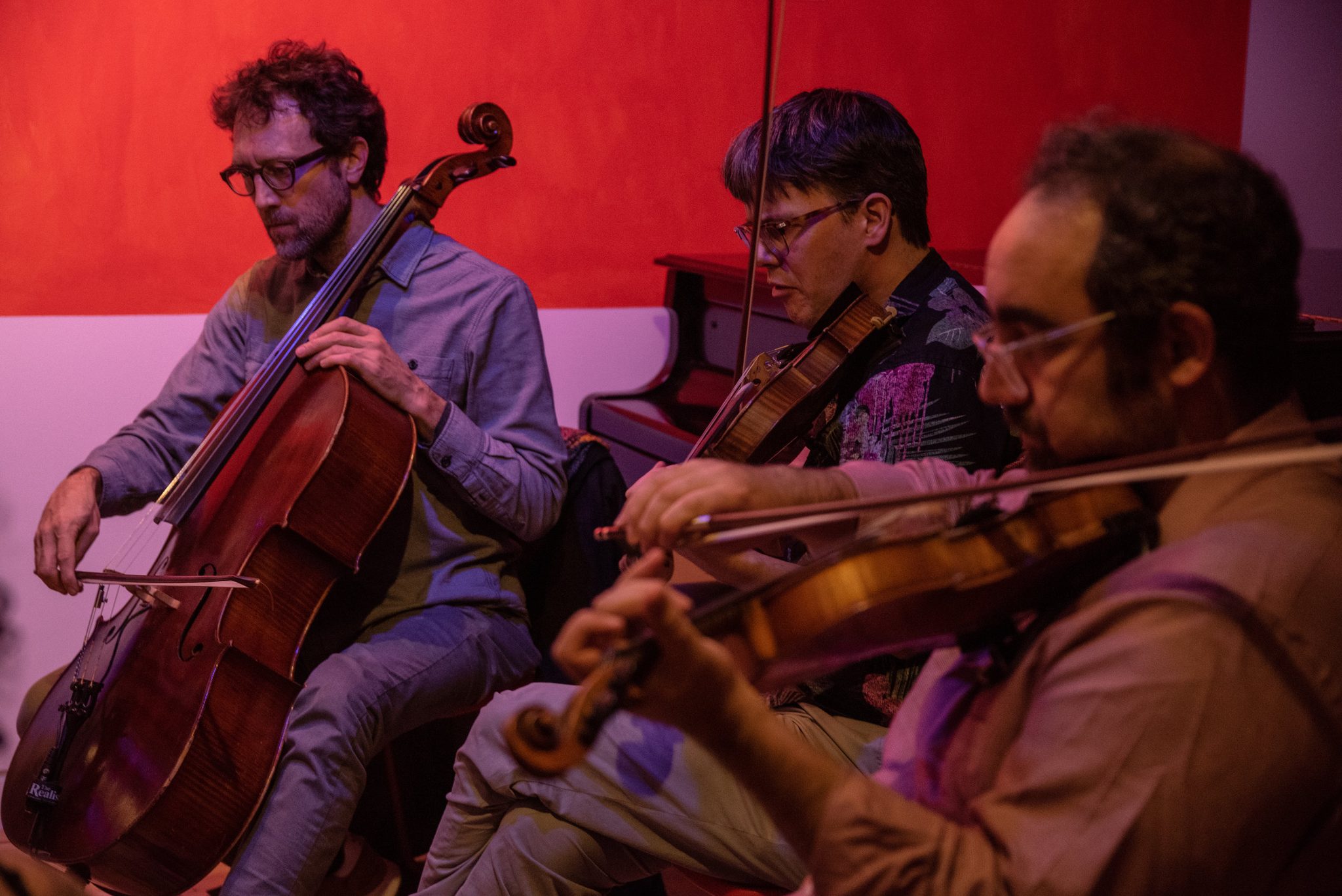 Strings in a red-lit room, cello and violins leaning into the same line.