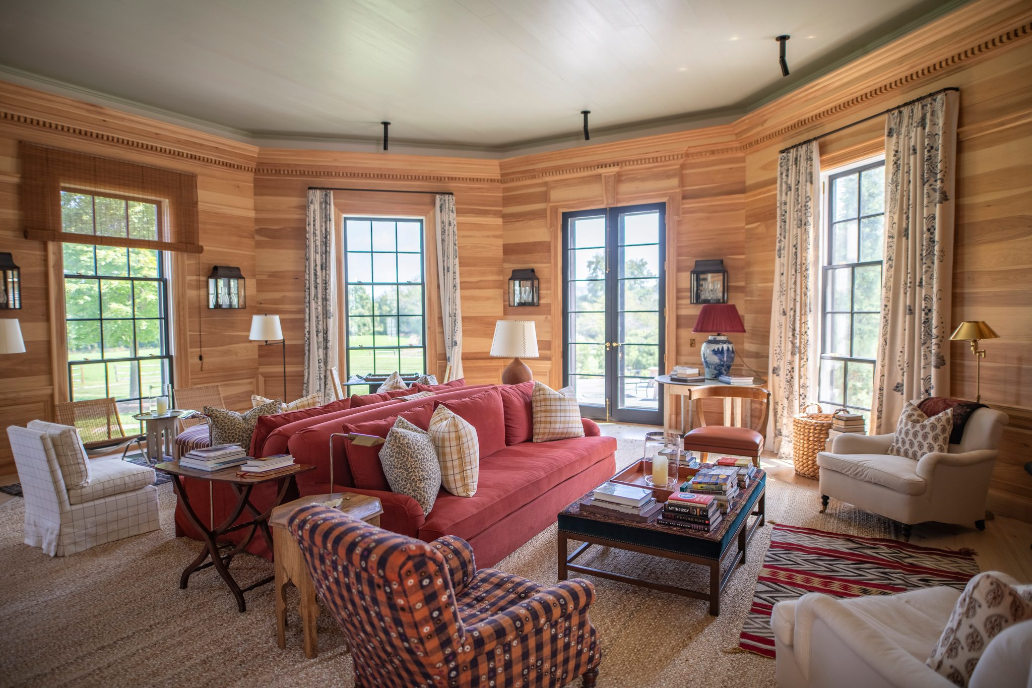 Honey-toned pine walls wrap an octagonal living room, and August light spills through tall windows onto a woven rug.
