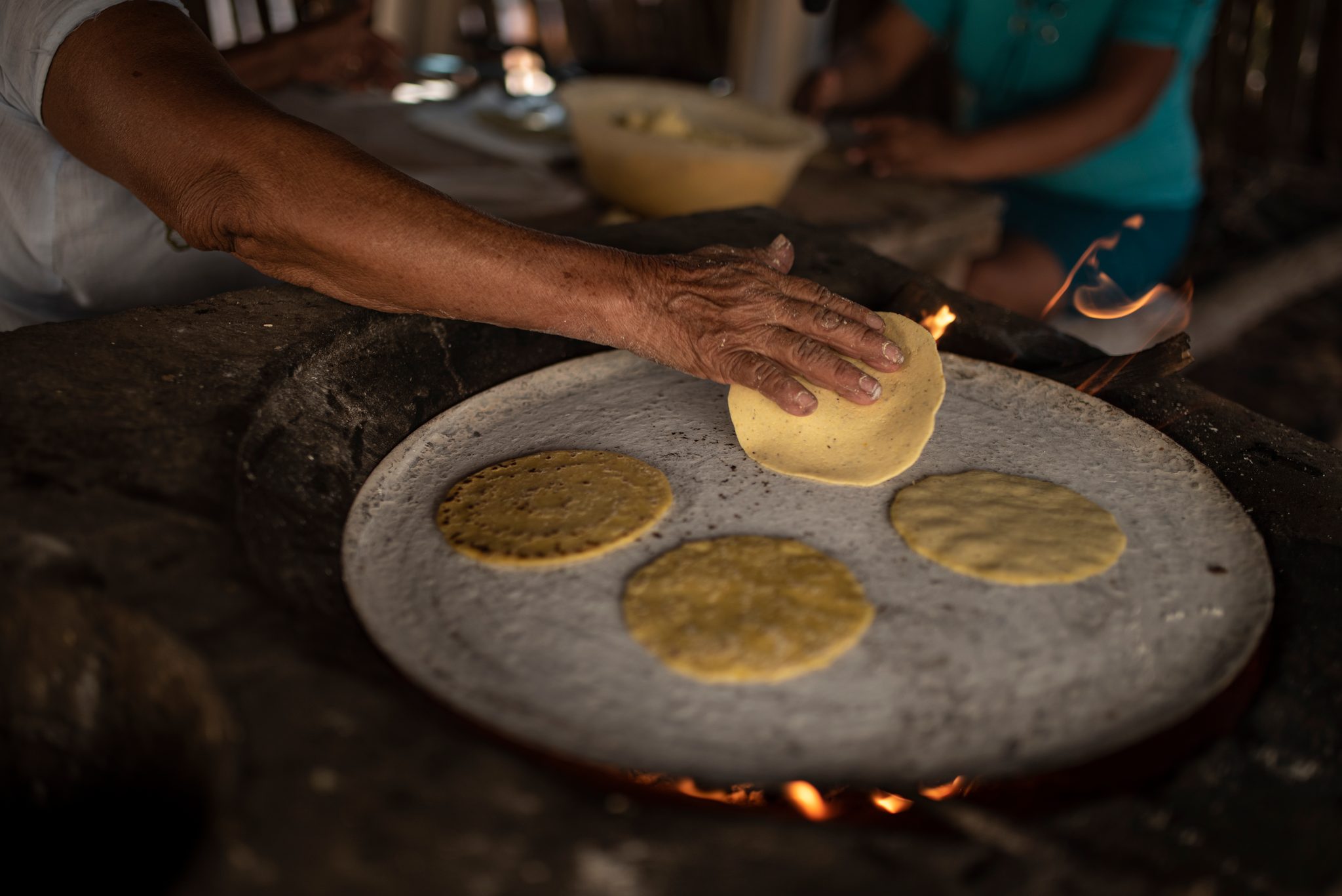 Fresh tortillas cook on the comal as she presses out another.